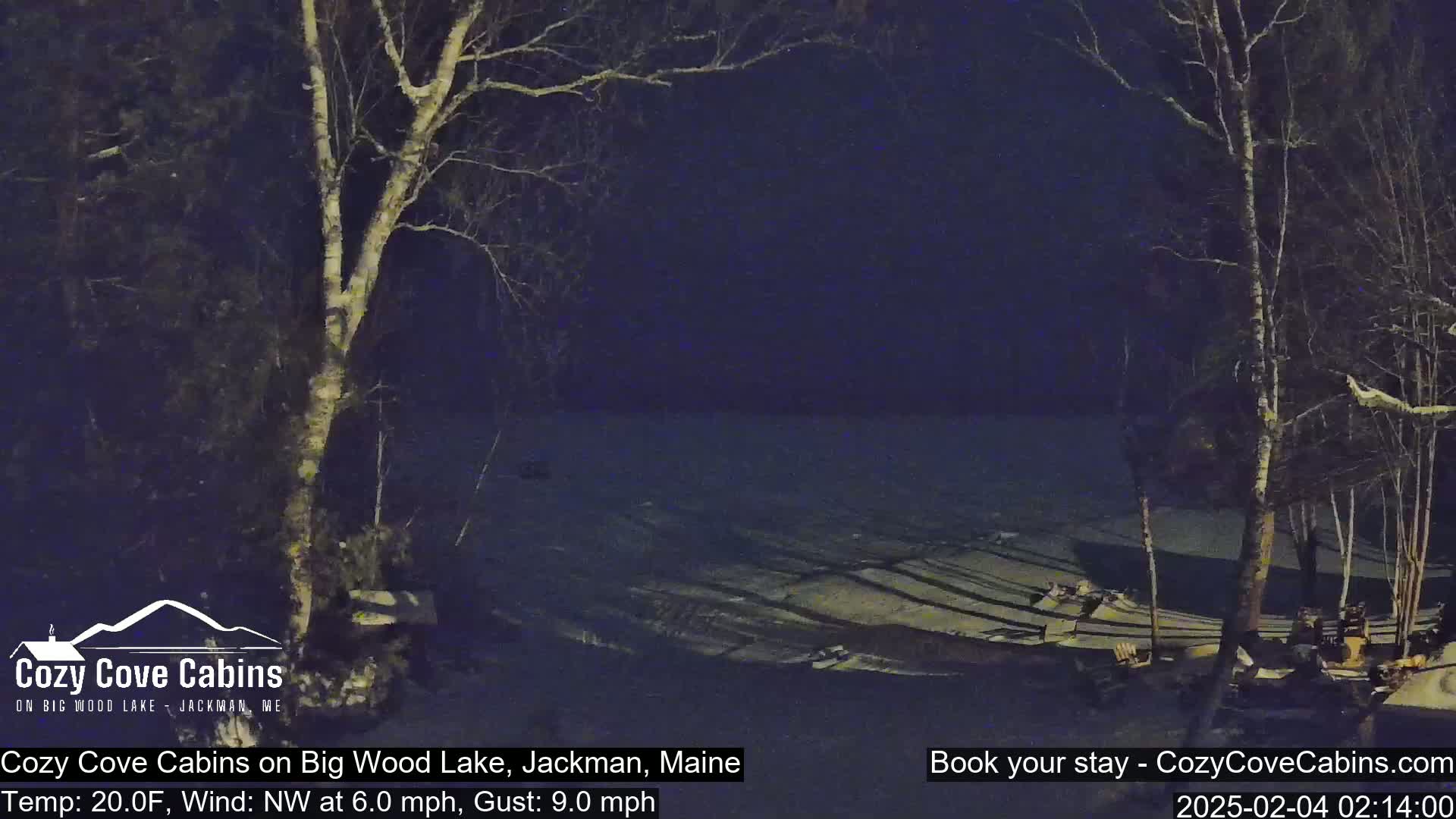 A nighttime view of a snow-covered lake shore with bare trees under a dark sky, a northwest wind at 6 mph with gusts up to 9 mph, and a temperature of 20°F.