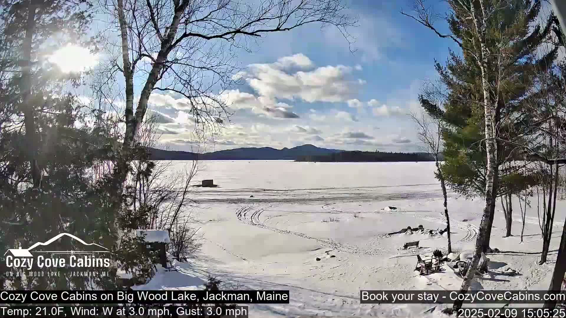 A snow-covered lake stretches to a distant mountain range under a partly sunny sky.