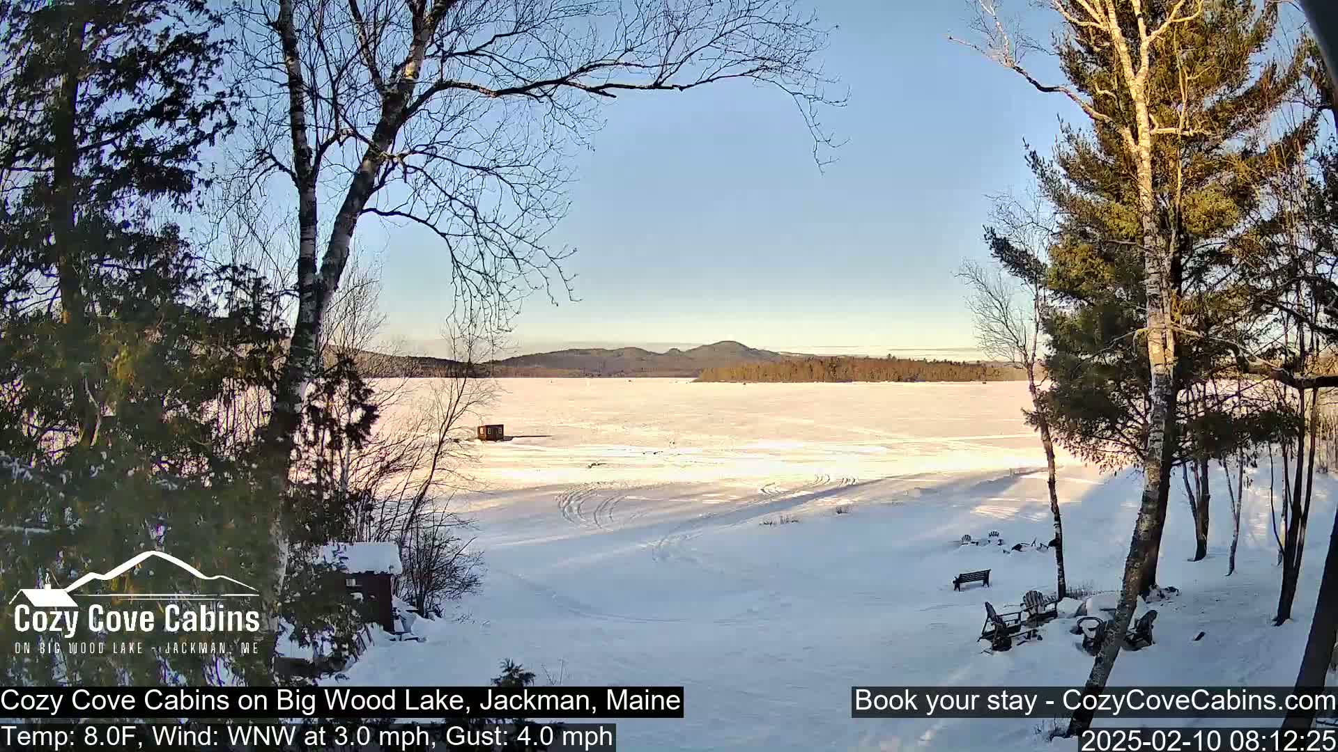 A snow-covered frozen lake stretches to a distant, tree-lined mountain range under a clear blue sky.