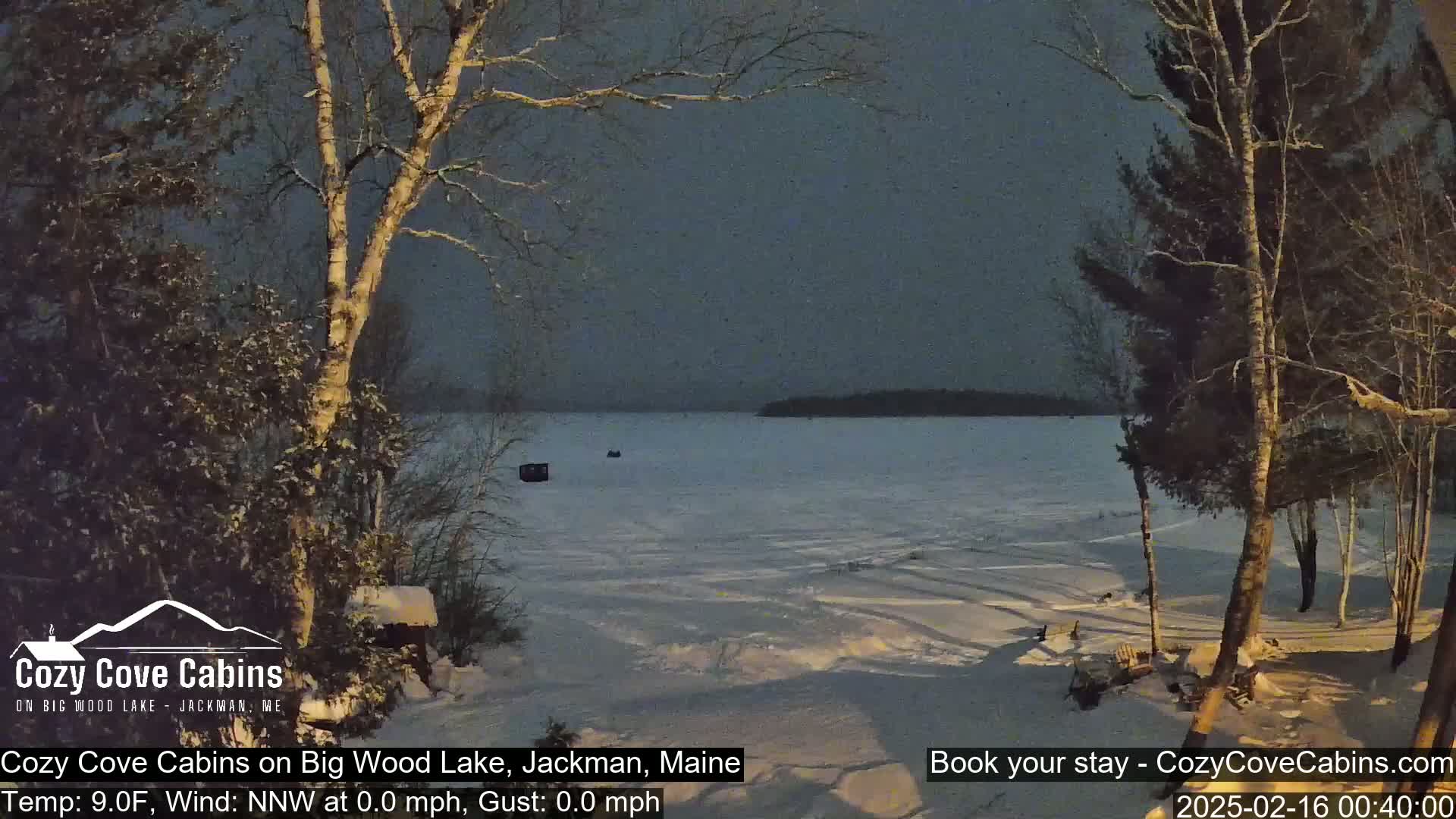 A snow-covered, frozen lake is visible at dusk, framed by snow-laden trees.