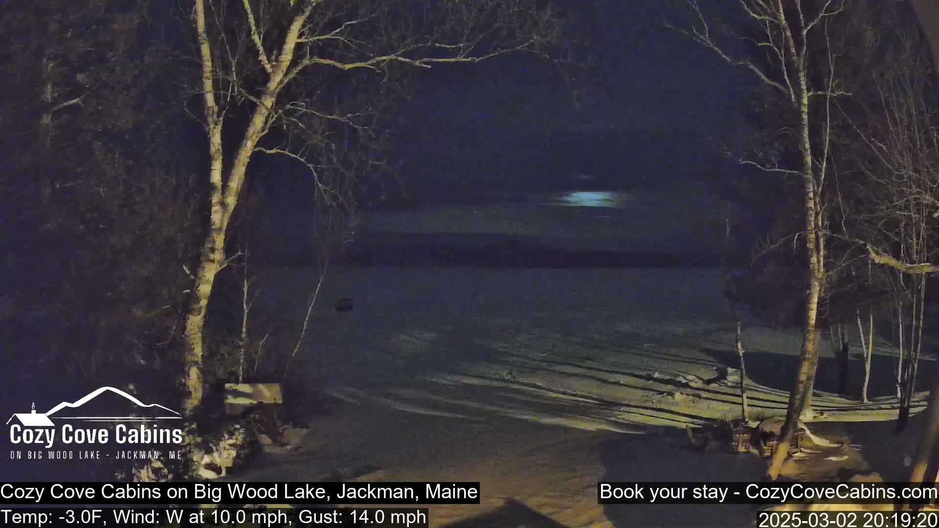 A nighttime view of a snow-covered lakeshore with bare trees under a partly cloudy sky, with a wind of 10 mph and gusts up to 14 mph and a temperature of -3°F.