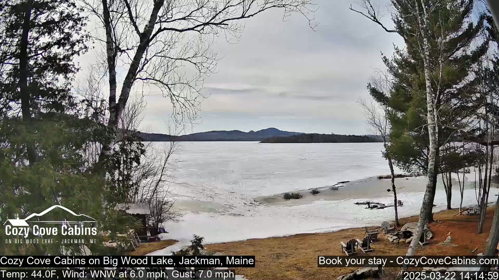 A partially frozen lake is visible from a lakeside property, with bare trees and a cloudy sky overhead.
