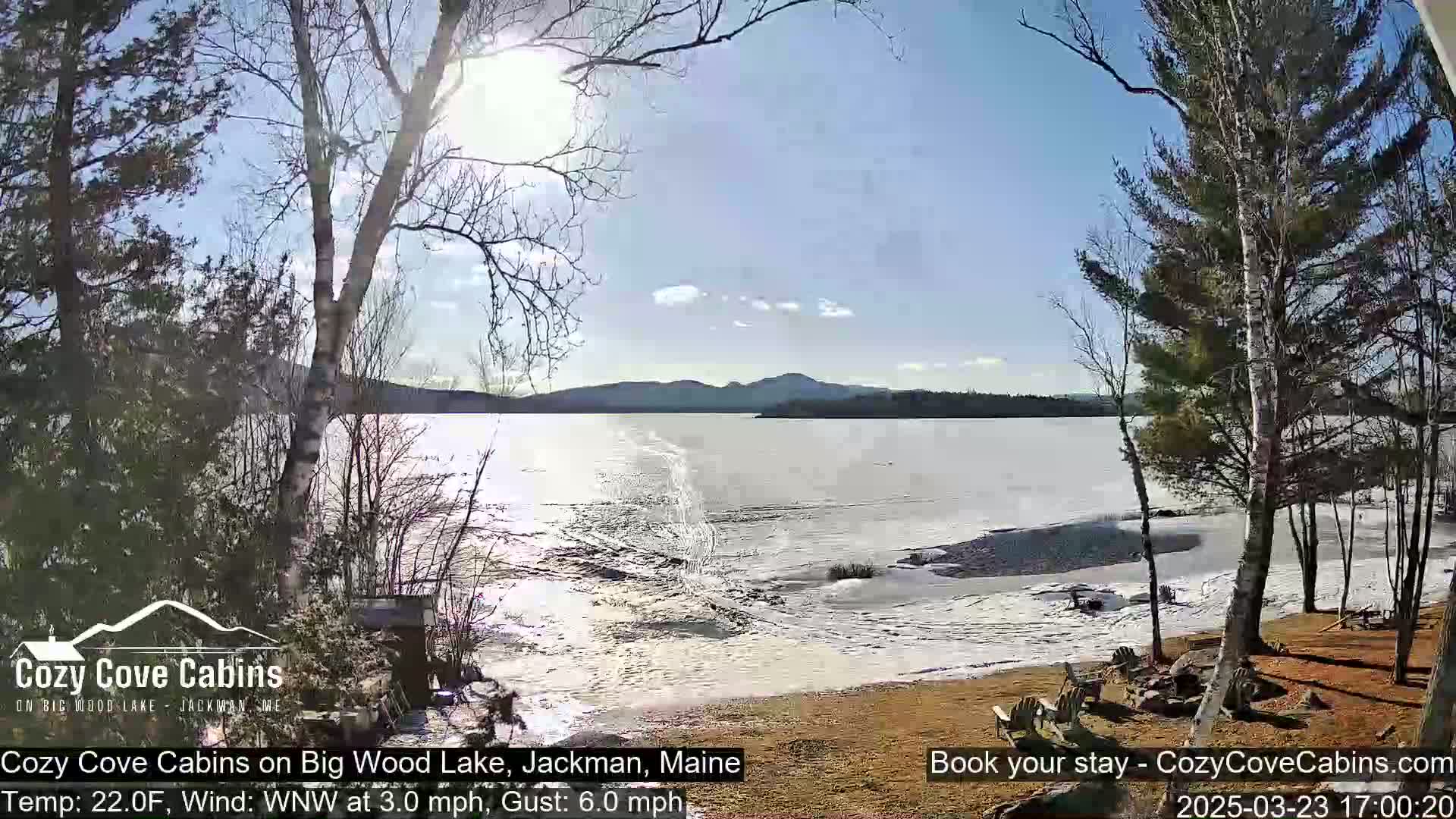 A partially frozen lake is seen from a lakeside property on a sunny day with a light wind.