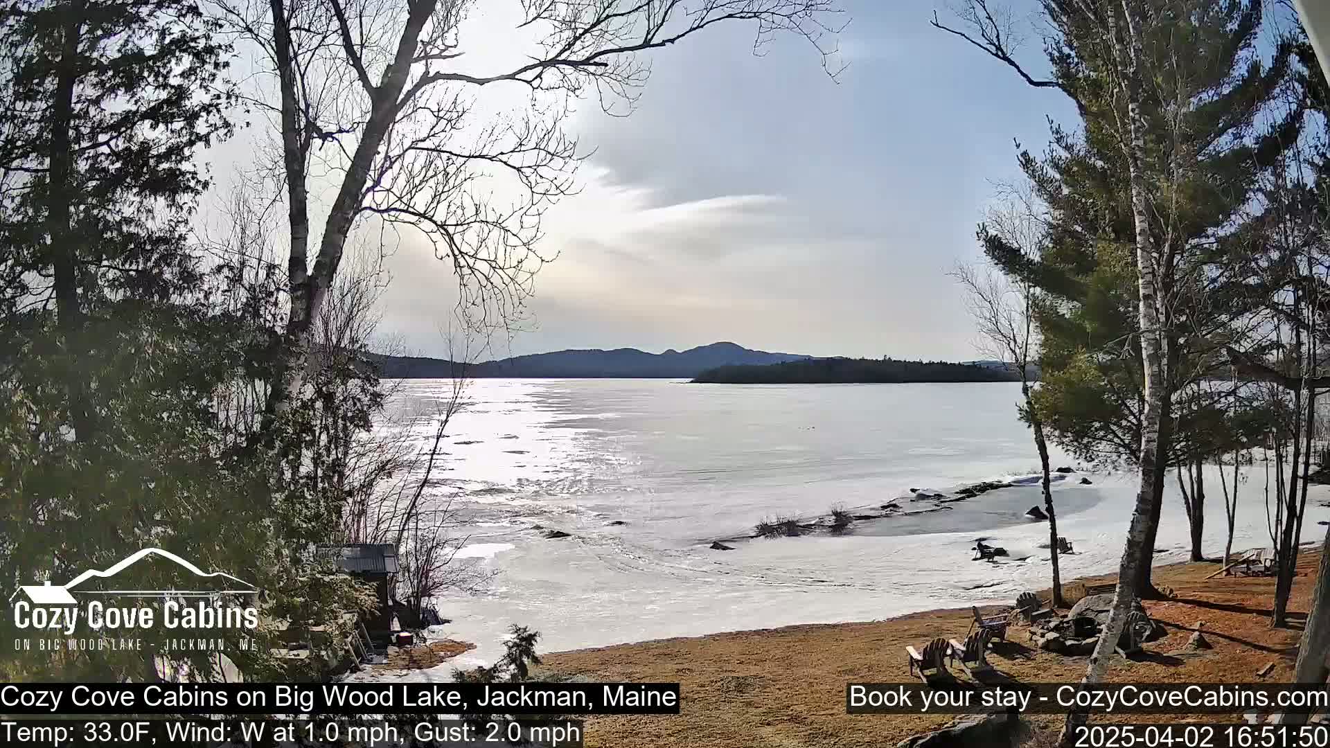 A partially frozen lake is visible from a lakeside property with bare trees under a partly cloudy sky.