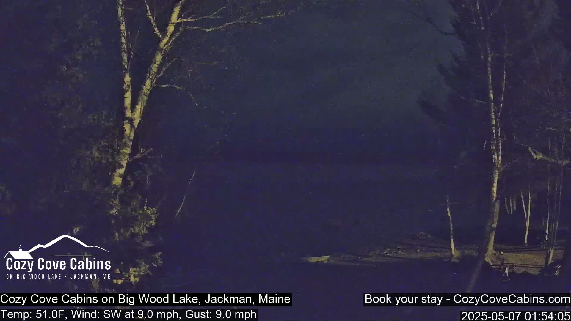 A nighttime view of a lake, surrounded by dark trees under a slightly cloudy sky, with a southwest wind blowing at 9 mph.