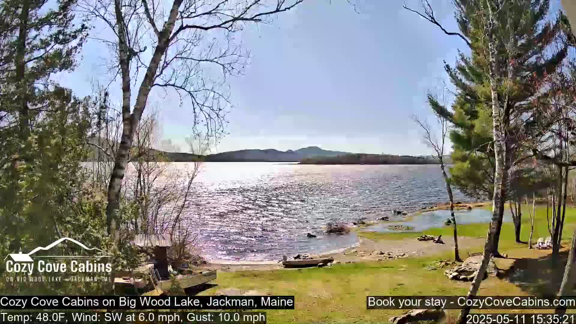 A calm lake is partially visible through trees under a mostly sunny sky, with a gentle southwest wind.