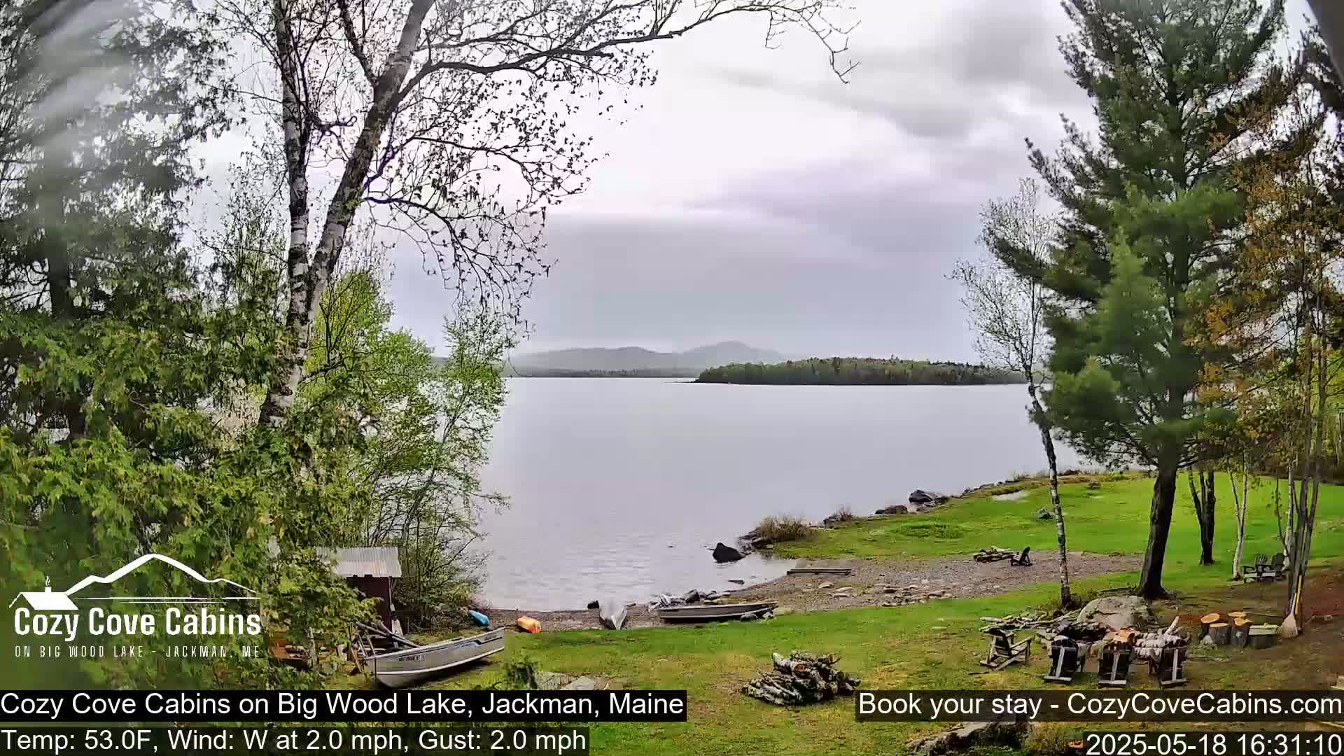 A calm lake with a rocky shoreline is partially obscured by trees under an overcast sky.