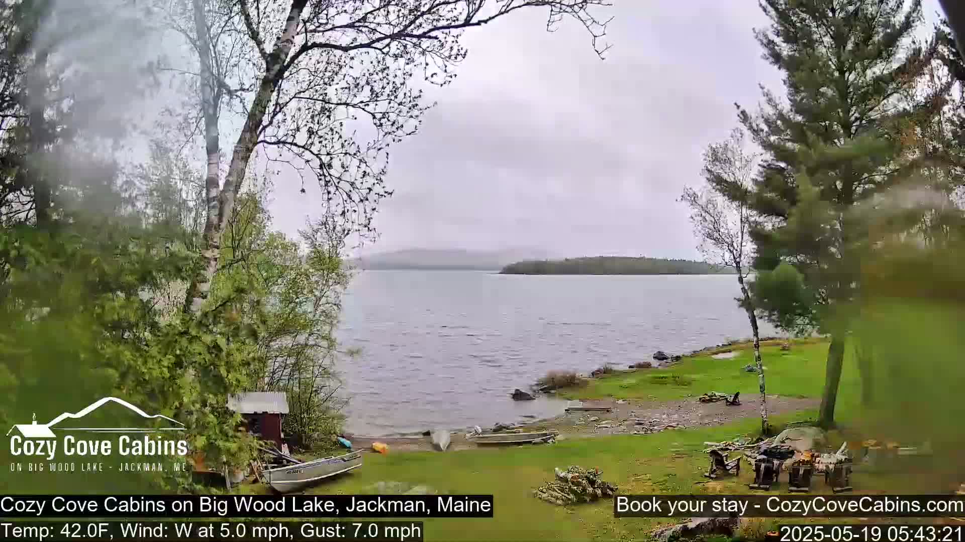 A lake with a rocky shoreline is seen from a lakeside yard on a cloudy day with a westerly wind.