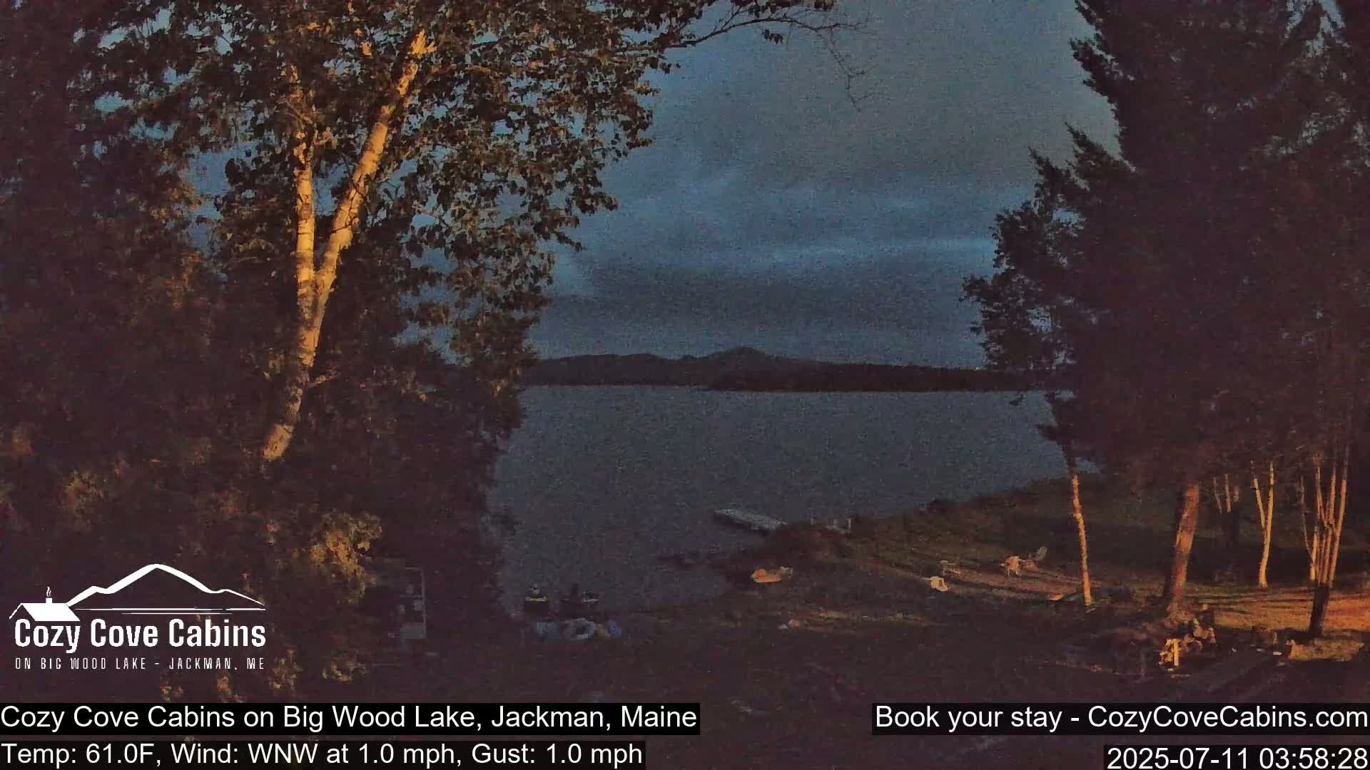 A tranquil lake scene at dusk, with trees silhouetted against a dark sky, under calm conditions.