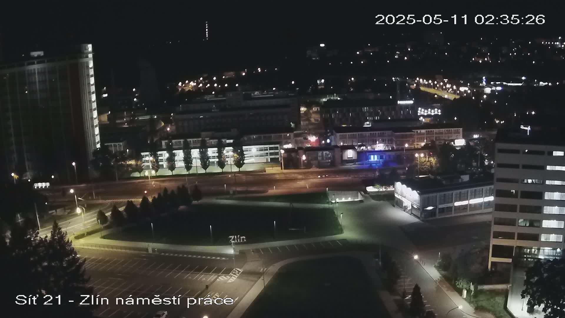 A nighttime aerial view of a city with illuminated buildings, roads, and a park-like area.