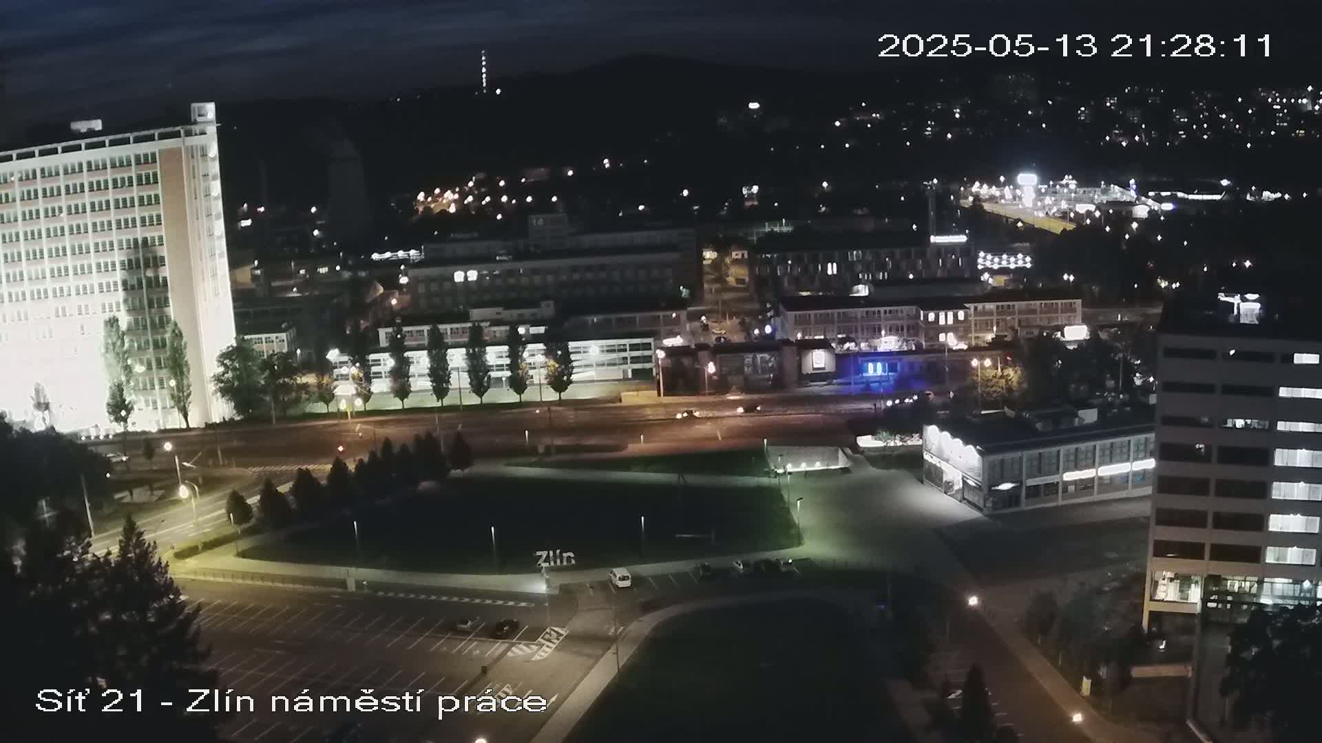 A nighttime aerial view of a city, showing brightly lit buildings and streets, with a few cars visible.