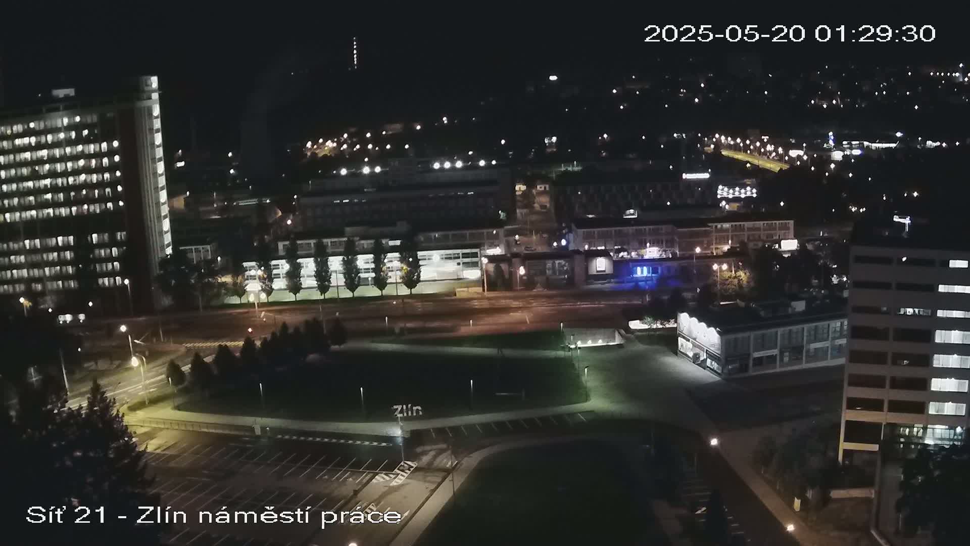 A nighttime aerial view of a city showing streets, buildings, and a park, with lights illuminating the scene.