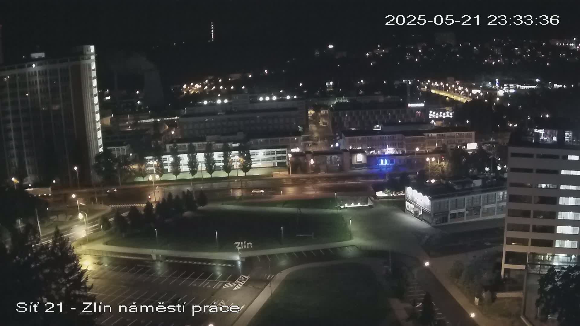 A nighttime aerial view of a city showing wet streets, buildings with lights, and a few vehicles.