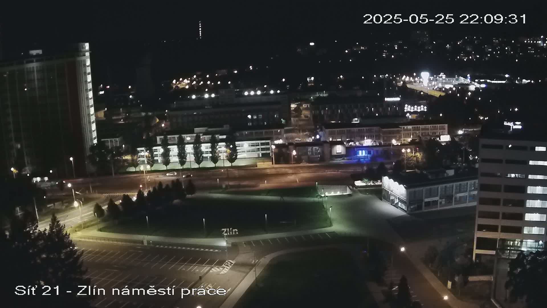 A nighttime aerial view of a city with illuminated streets, buildings, and a park, under clear skies.