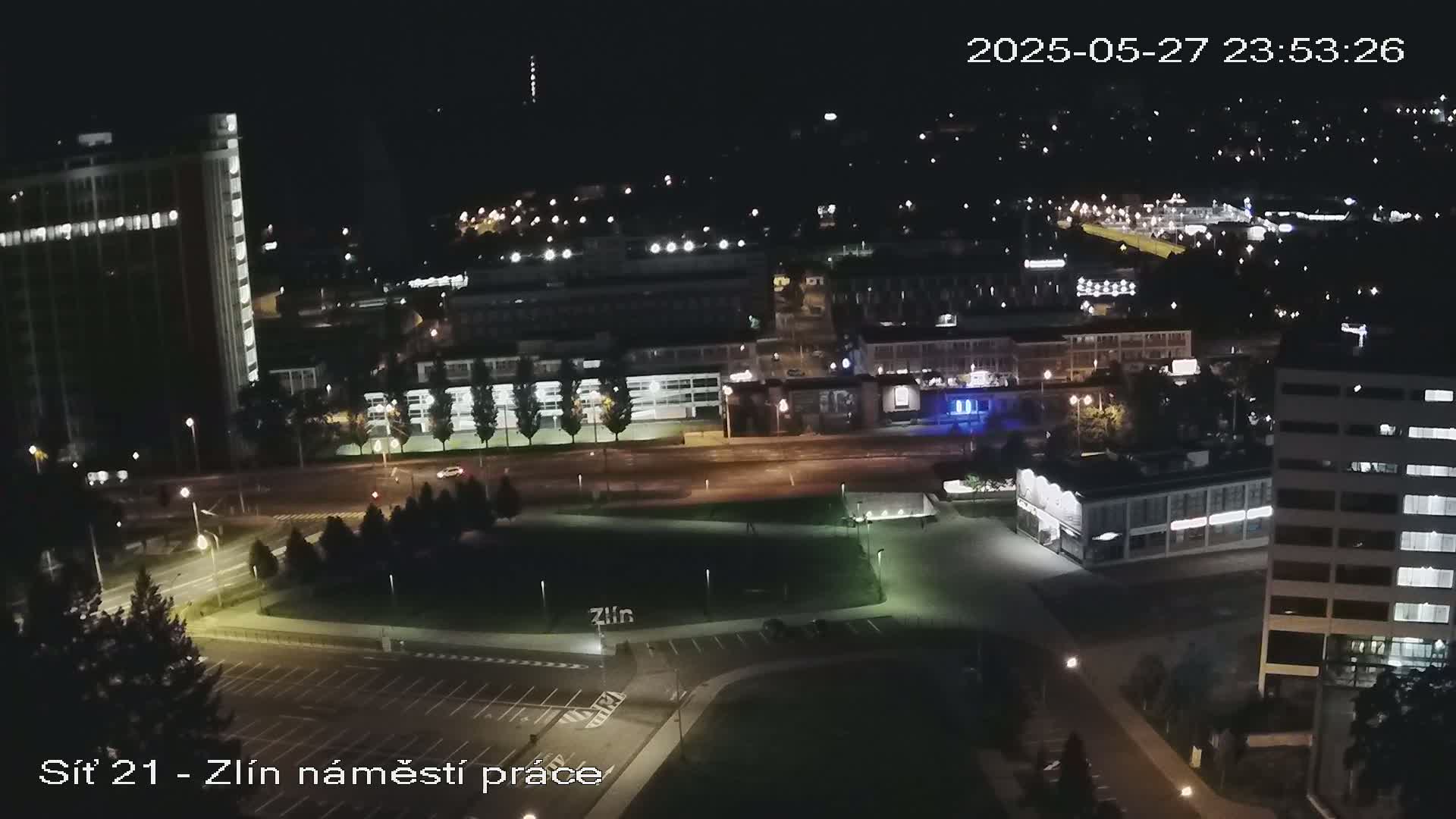 A nighttime aerial view of a city showing buildings, roads, and a park with minimal traffic.