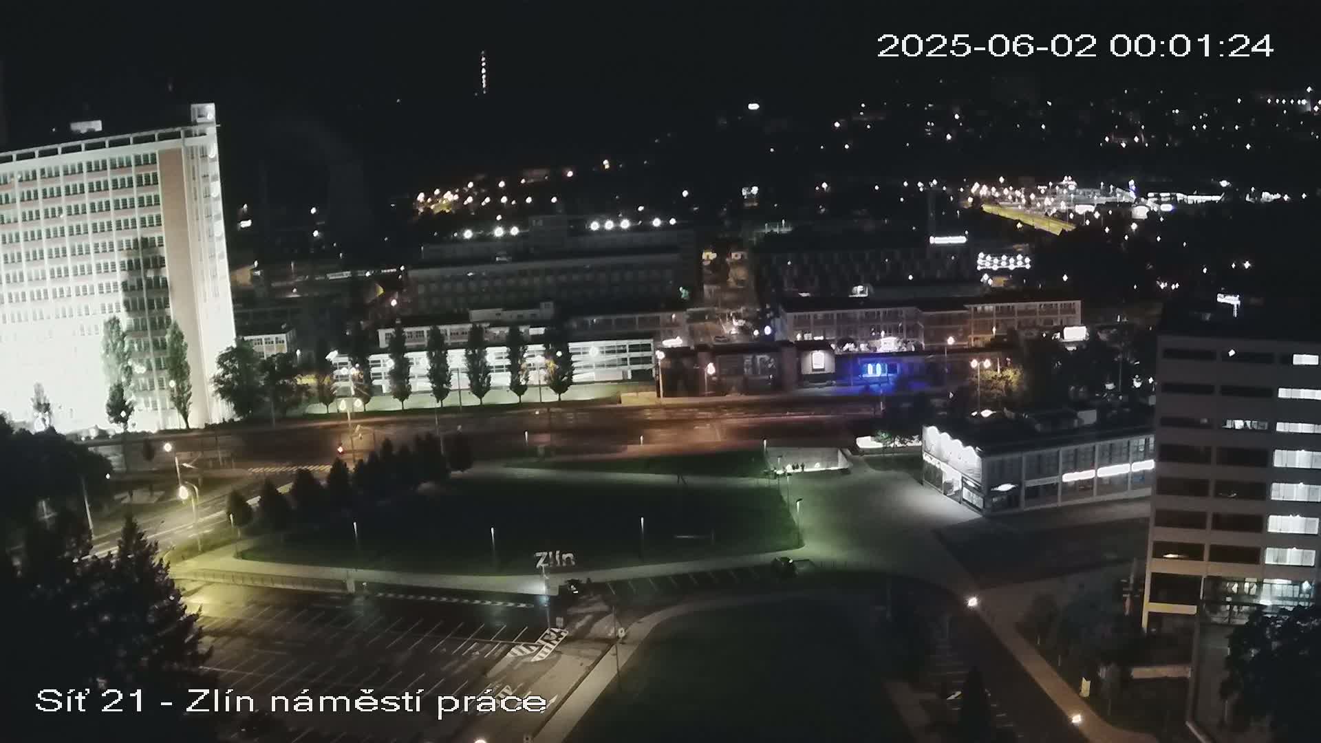A nighttime aerial view of a city, showing illuminated buildings, streets, and a park, under clear skies.