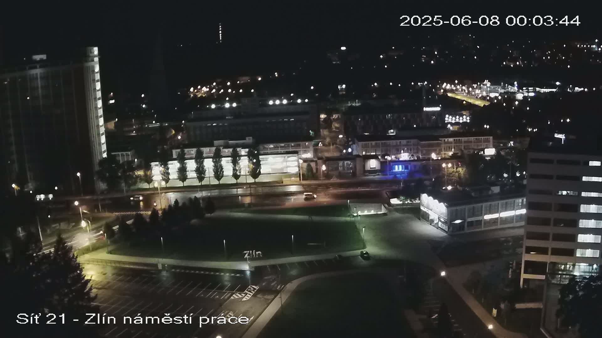 A nighttime aerial view of a city with wet streets and sparsely lit buildings and parking lots.