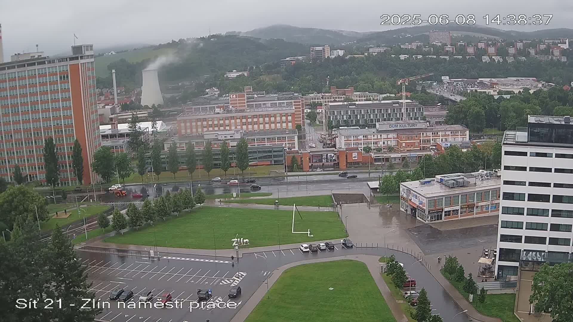 A high-angle, wide view of a city with several buildings and a large grassy area on a rainy day.