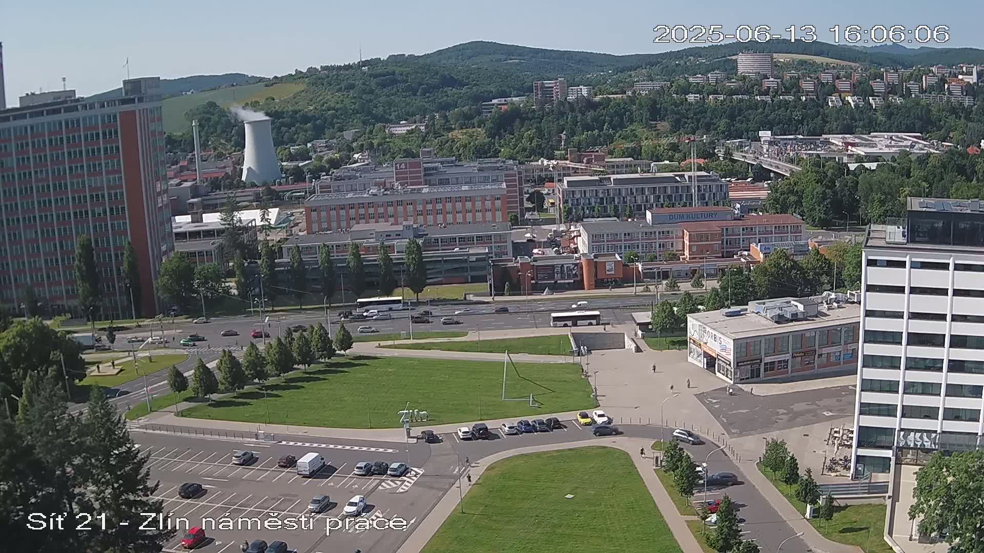 A high-angle view of a city square with a parking lot, surrounded by buildings under a clear, sunny sky.