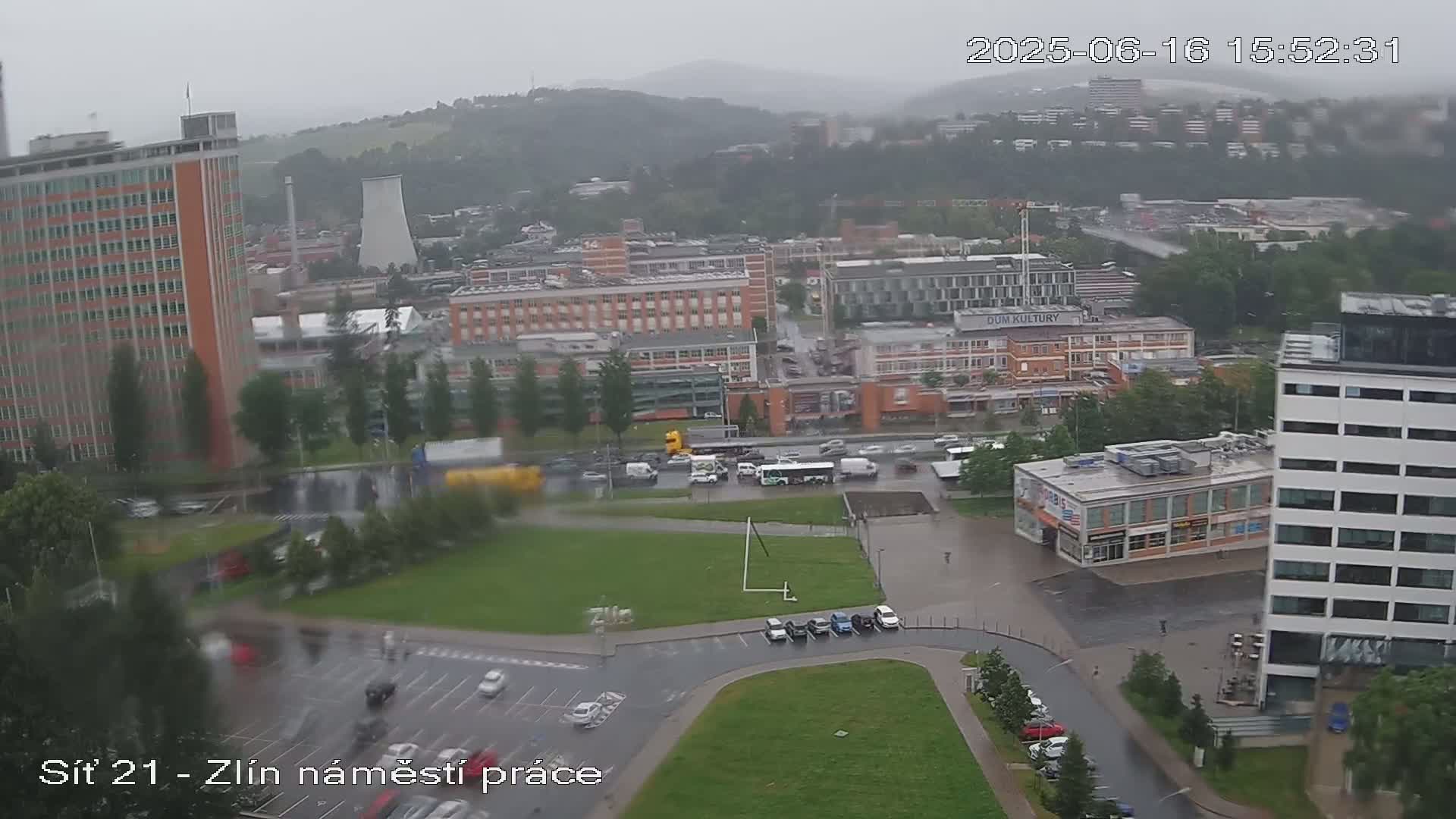 A high-angle view of a city square with buildings and vehicles on a rainy day.