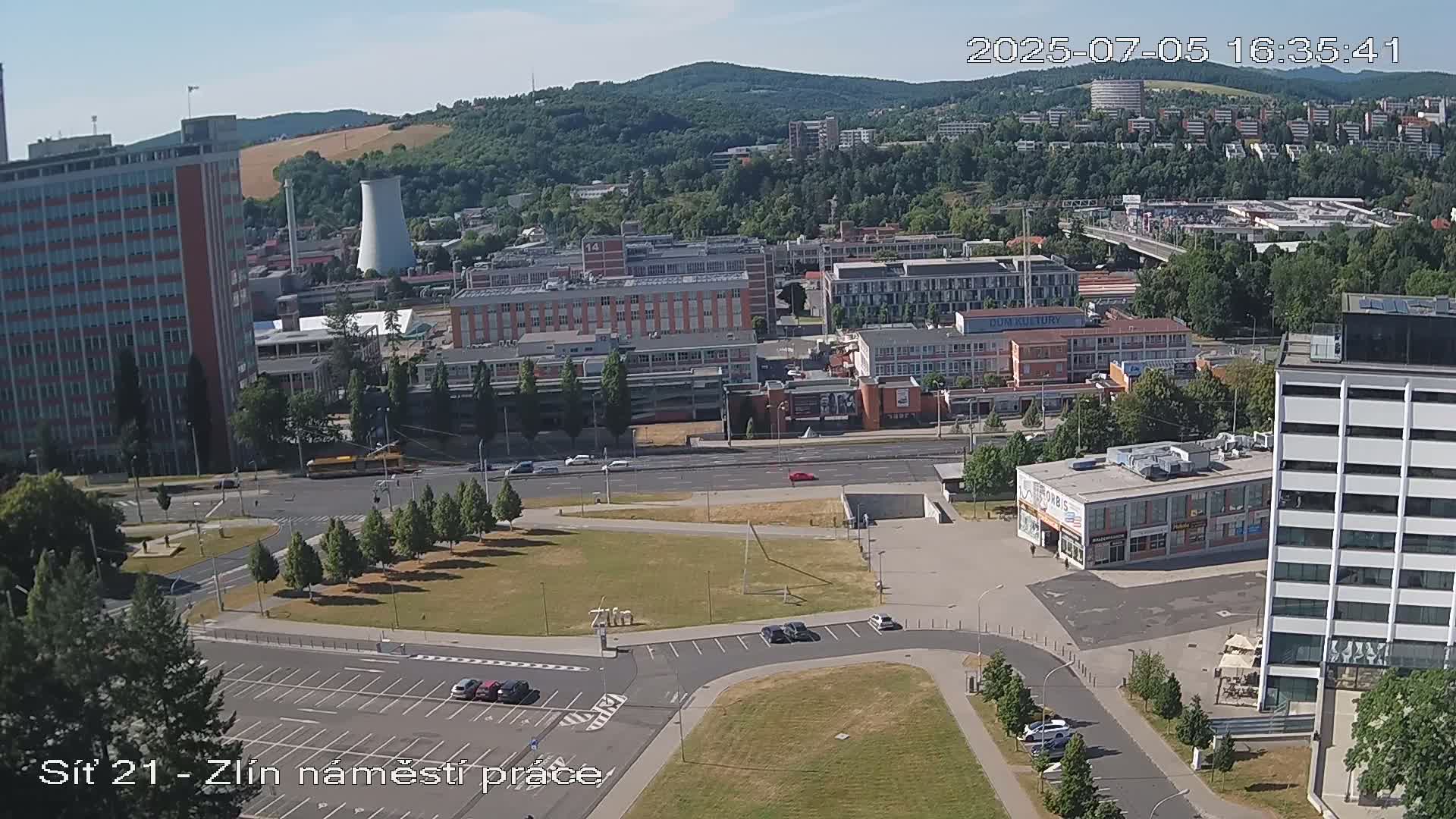 An aerial view shows a city block with several multi-story buildings under a clear, sunny sky.