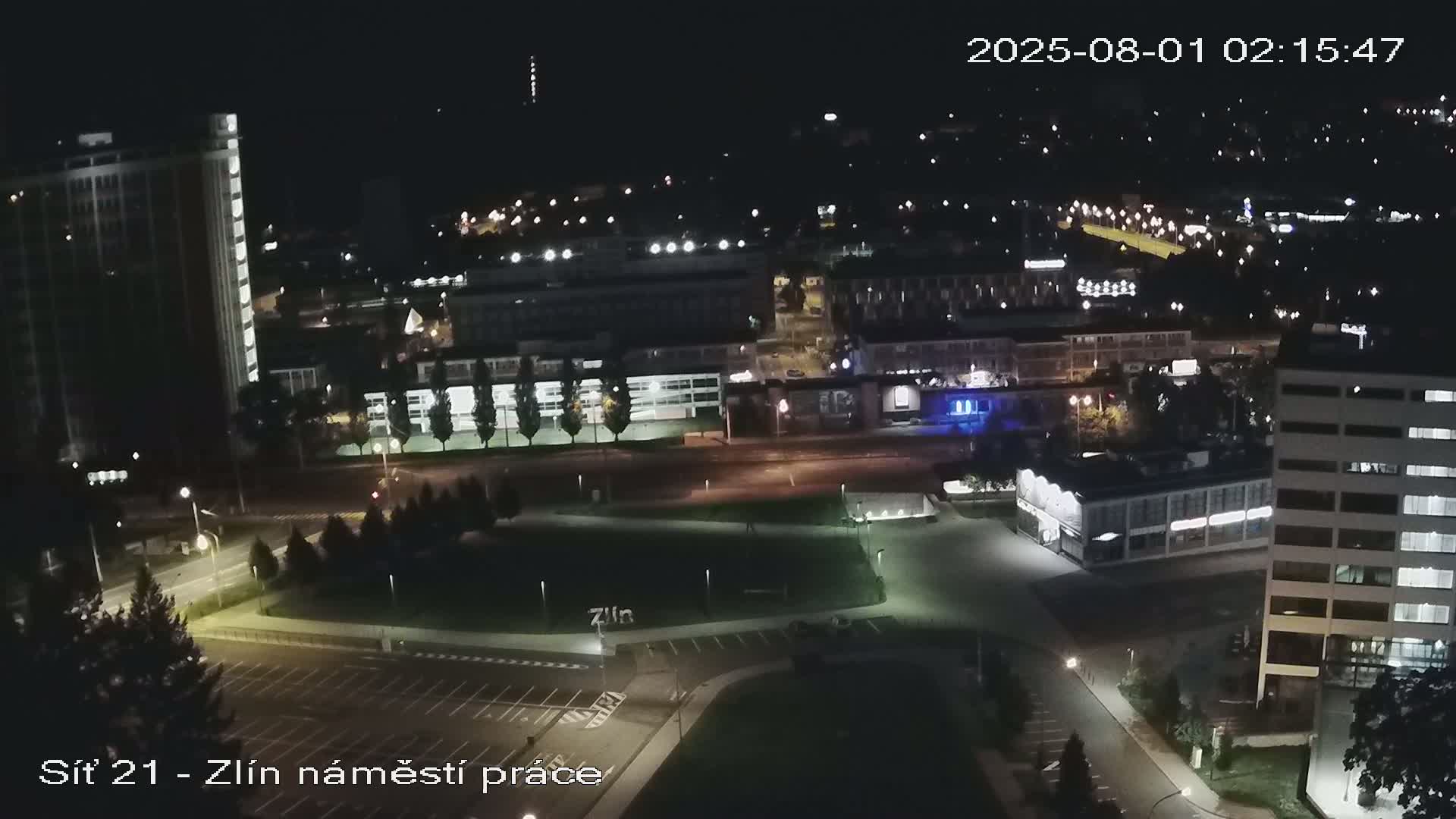 A nighttime aerial view of a city with illuminated buildings, roads, and a park-like area.
