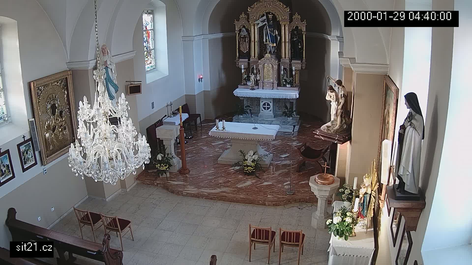 A church interior with a marble floor, an altar, religious statues, and a large crystal chandelier is shown from an overhead perspective.