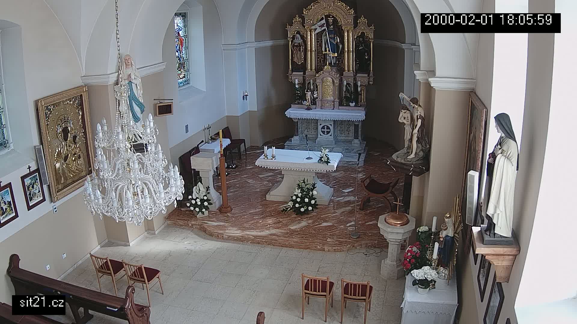An interior view of a church shows an altar, statues, a chandelier, and several pews.