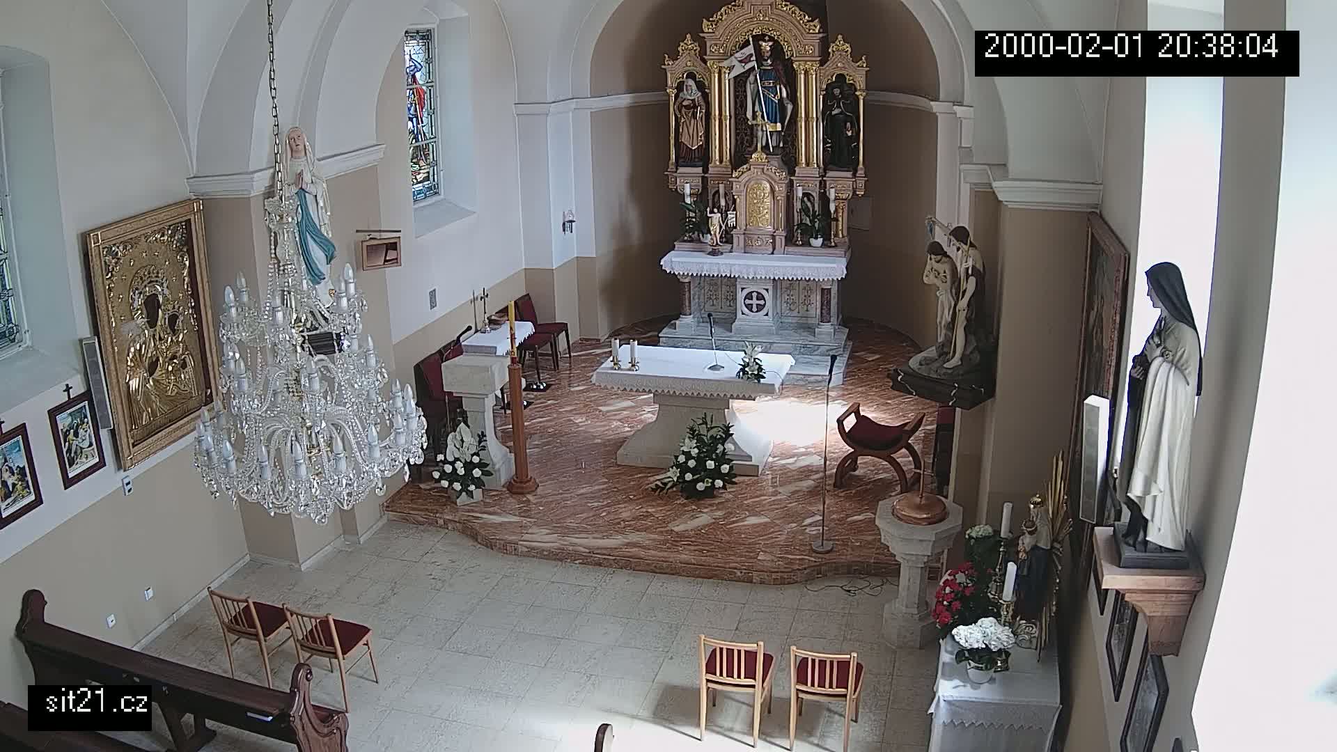 A church interior is shown, featuring an altar, several statues, a large chandelier, and empty chairs.