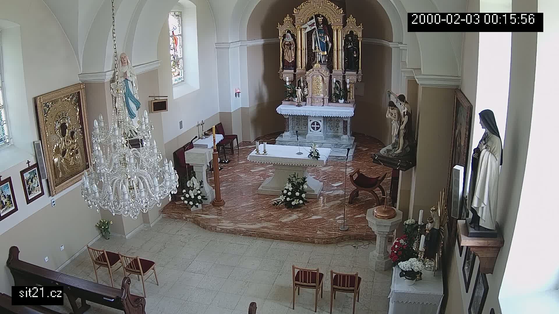 An indoor view of a church sanctuary, showing an altar, statues, a chandelier, and several chairs.