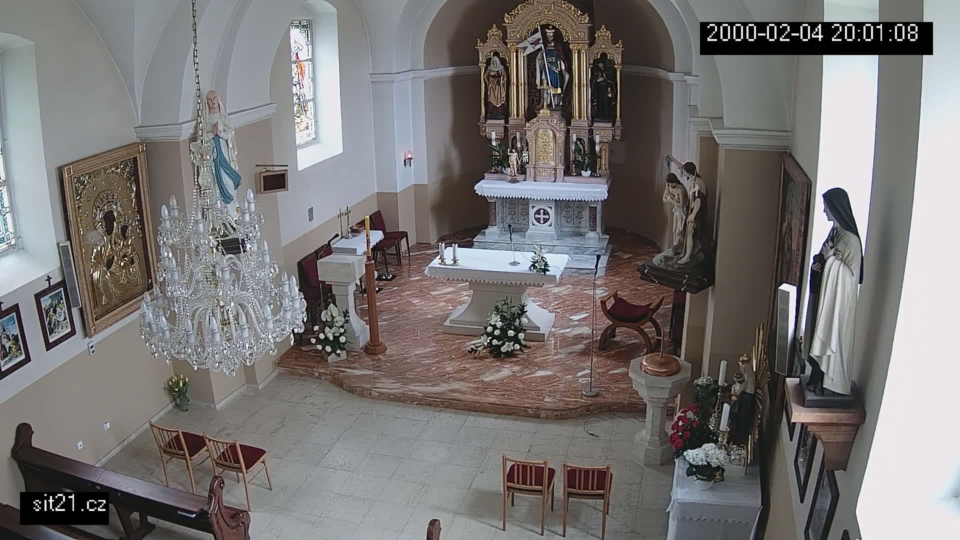 A church interior with marble flooring, an altar, several religious statues, a large crystal chandelier, and a few chairs.
