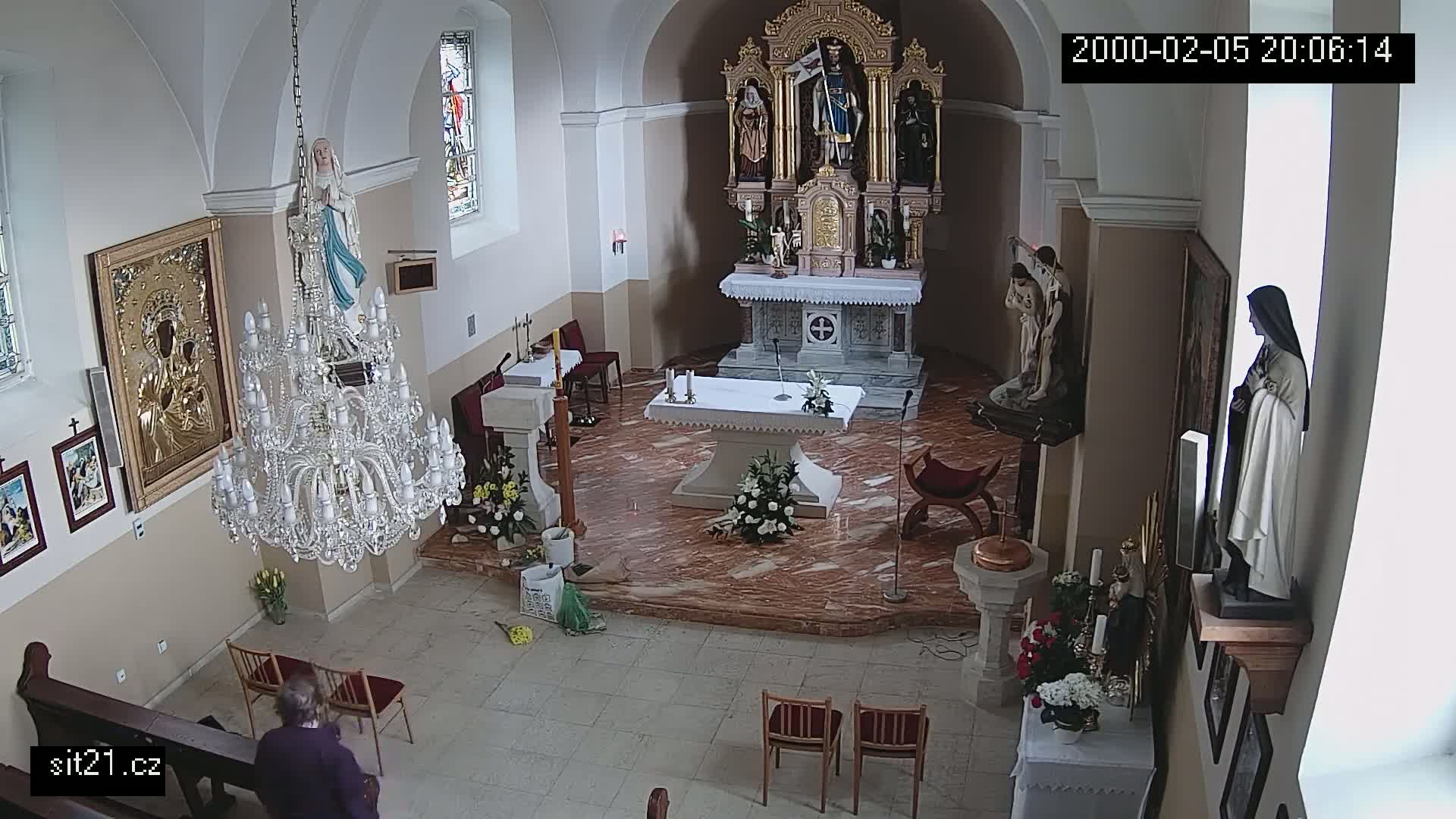 An indoor view of a church sanctuary, showing a marble floor, altar, statues, a large chandelier, and a person standing near the back.
