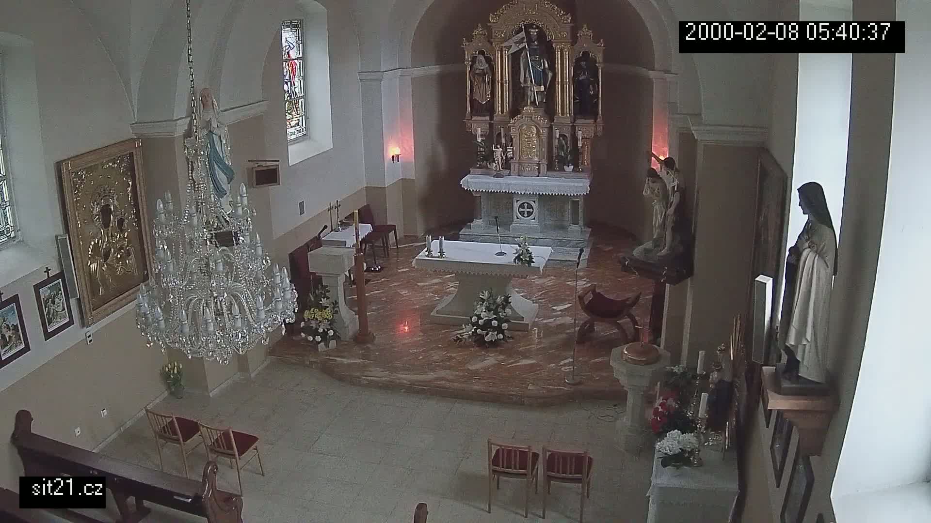 An indoor view of a church sanctuary with marble floors, religious statues, a large crystal chandelier, and floral arrangements on the altar and side tables.