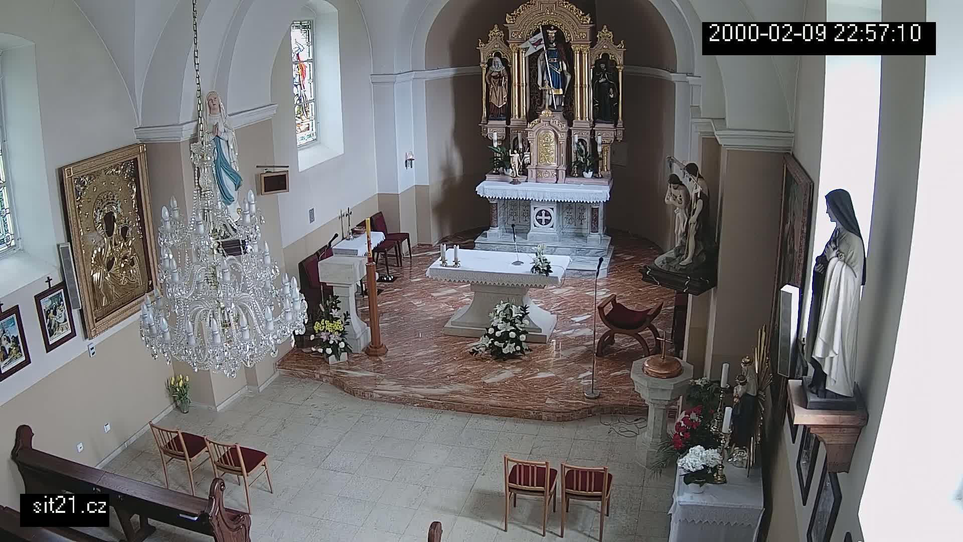 An indoor view of a church sanctuary with a marble altar, a large crystal chandelier, religious statues, and several floral arrangements.