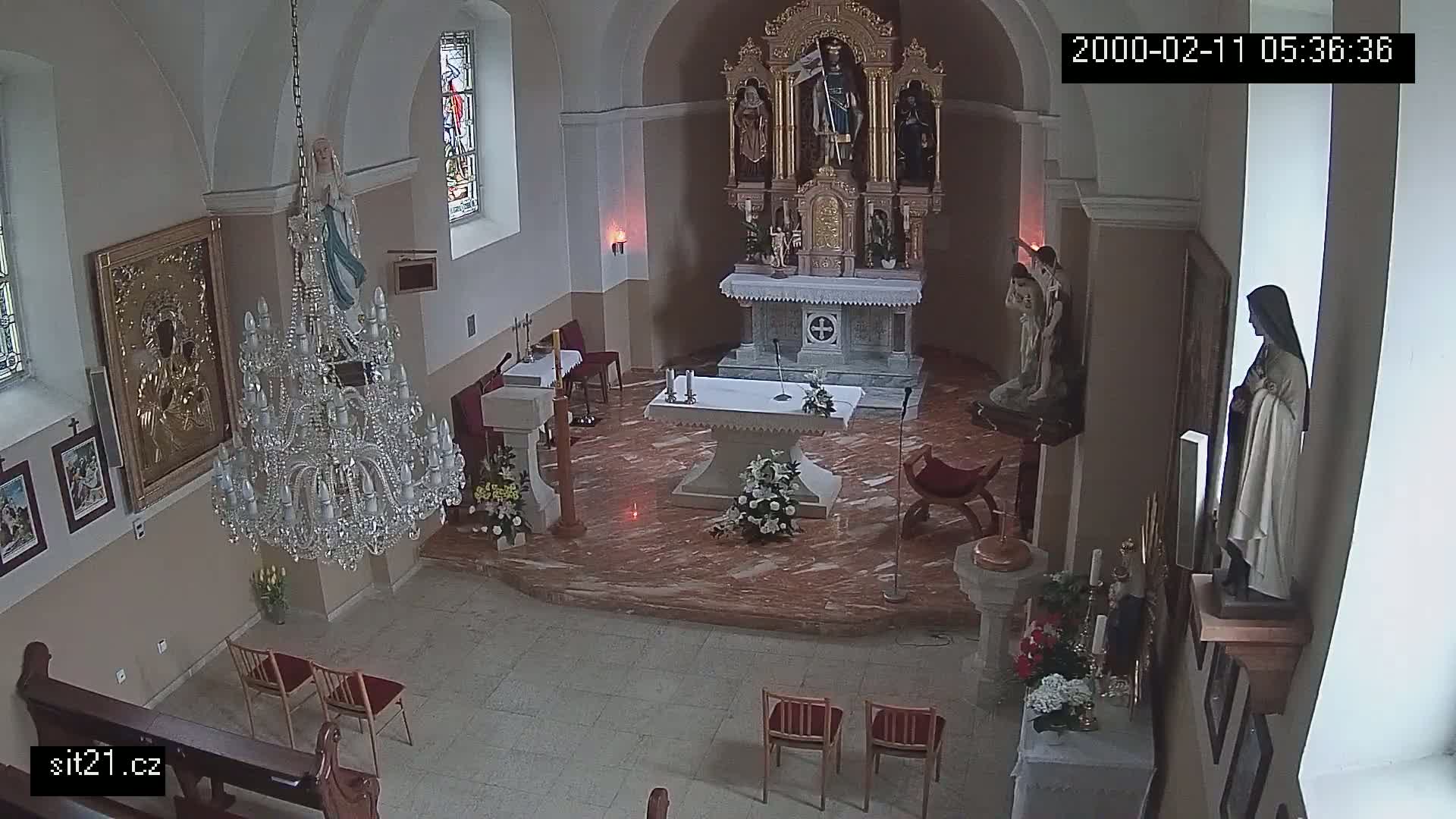 An indoor view of a church sanctuary showing an altar, several religious statues, a large chandelier, and a few chairs.