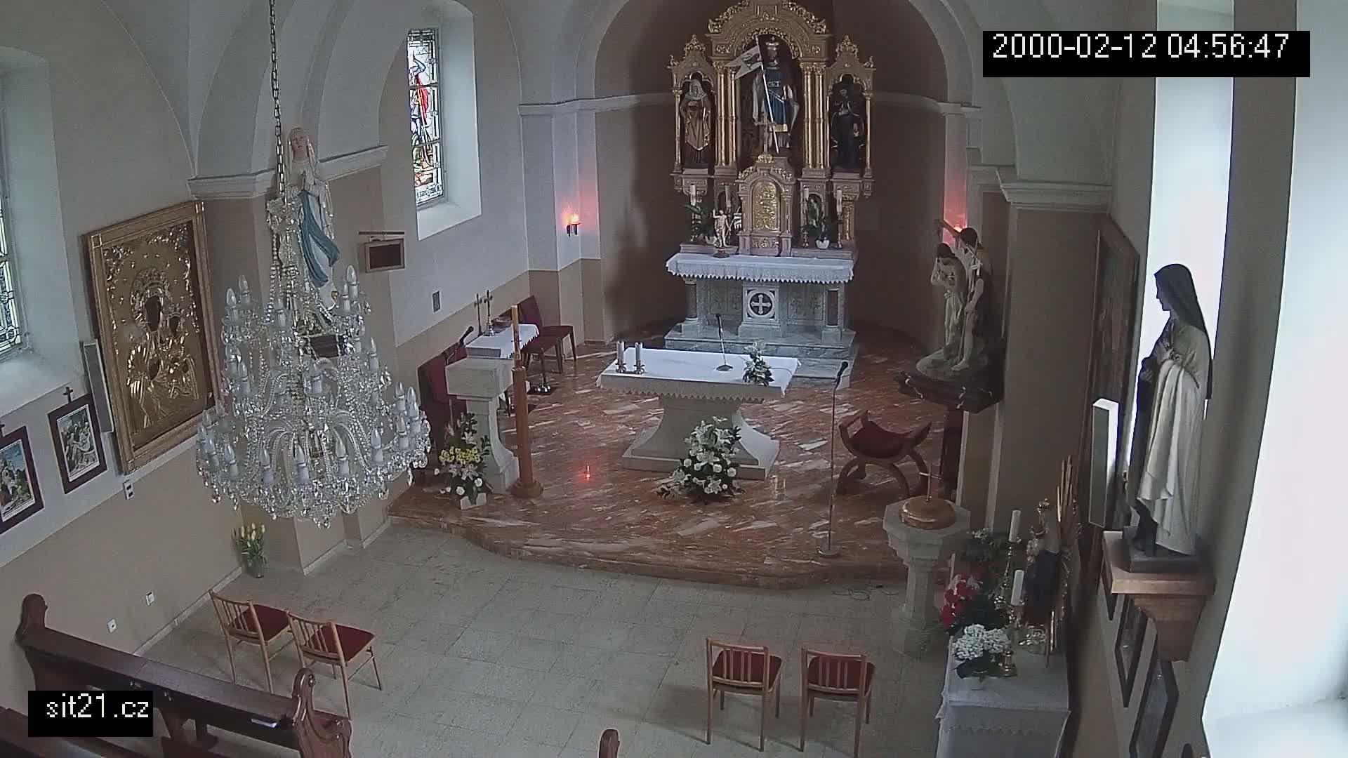 An indoor view of a church sanctuary, featuring an altar, religious statues, a chandelier, and several chairs.