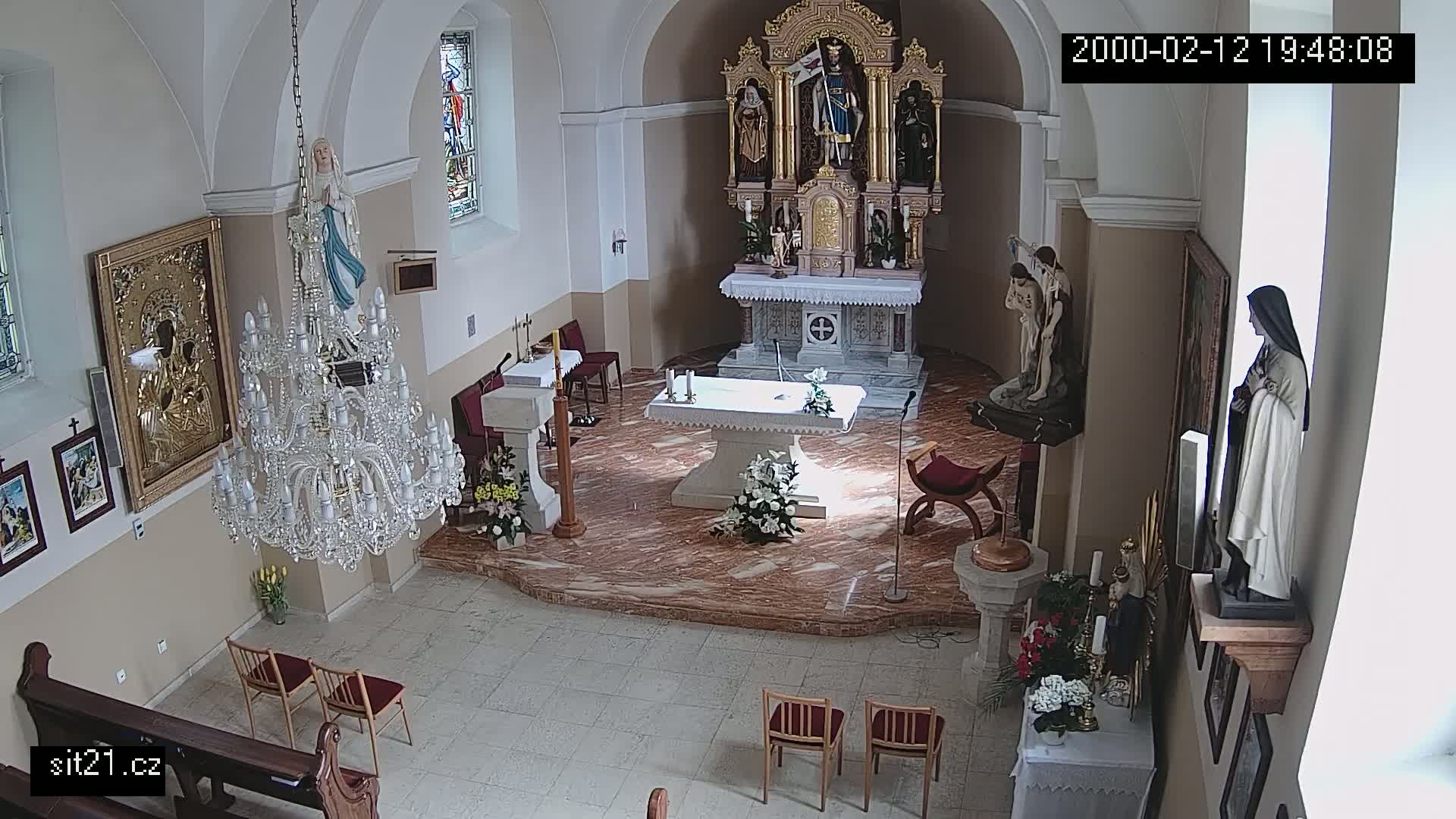 An indoor view of a church sanctuary, featuring an altar, statues, a large chandelier, and several chairs.