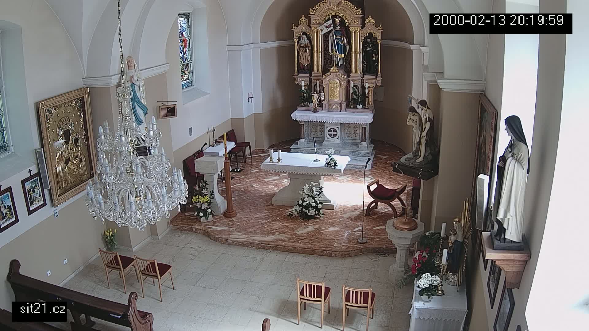An indoor church sanctuary with marble floors, religious statues, a large crystal chandelier, and several floral arrangements.