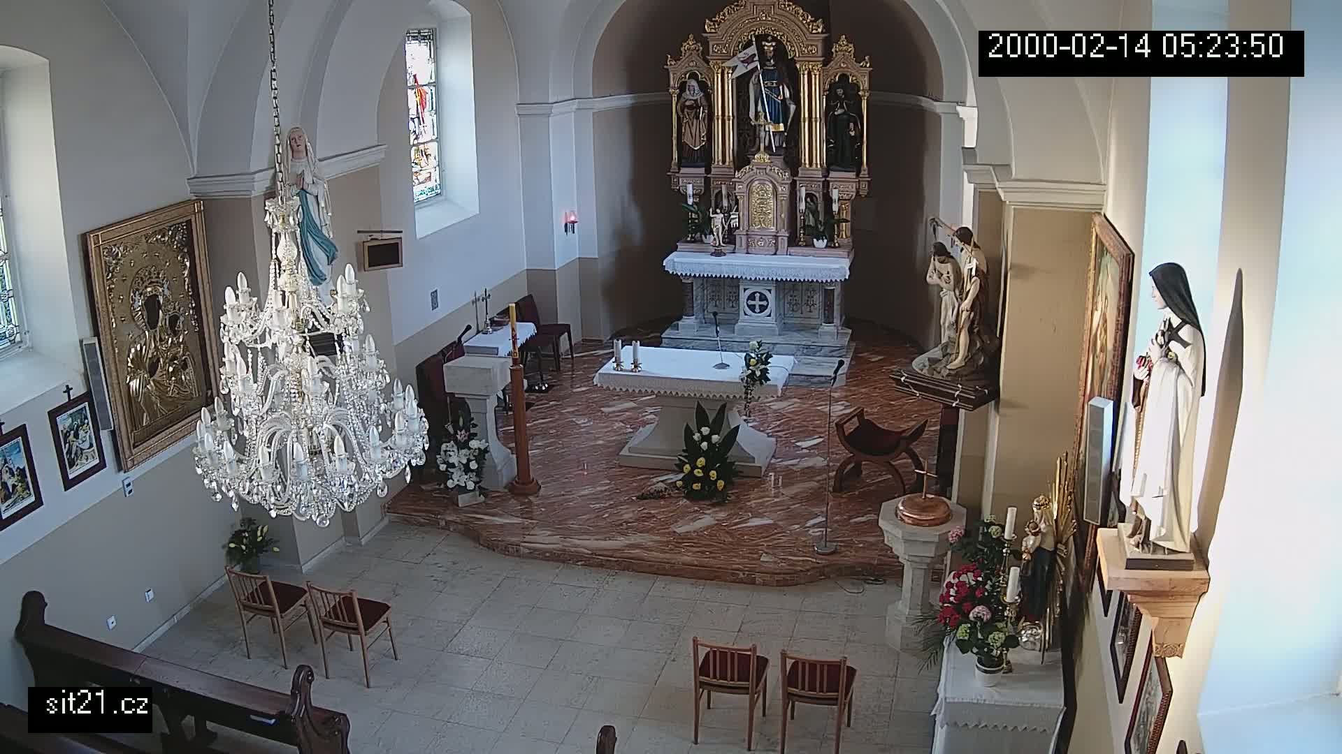 A church interior with a marble floor, ornate altar, statues, and a large crystal chandelier, brightly lit.