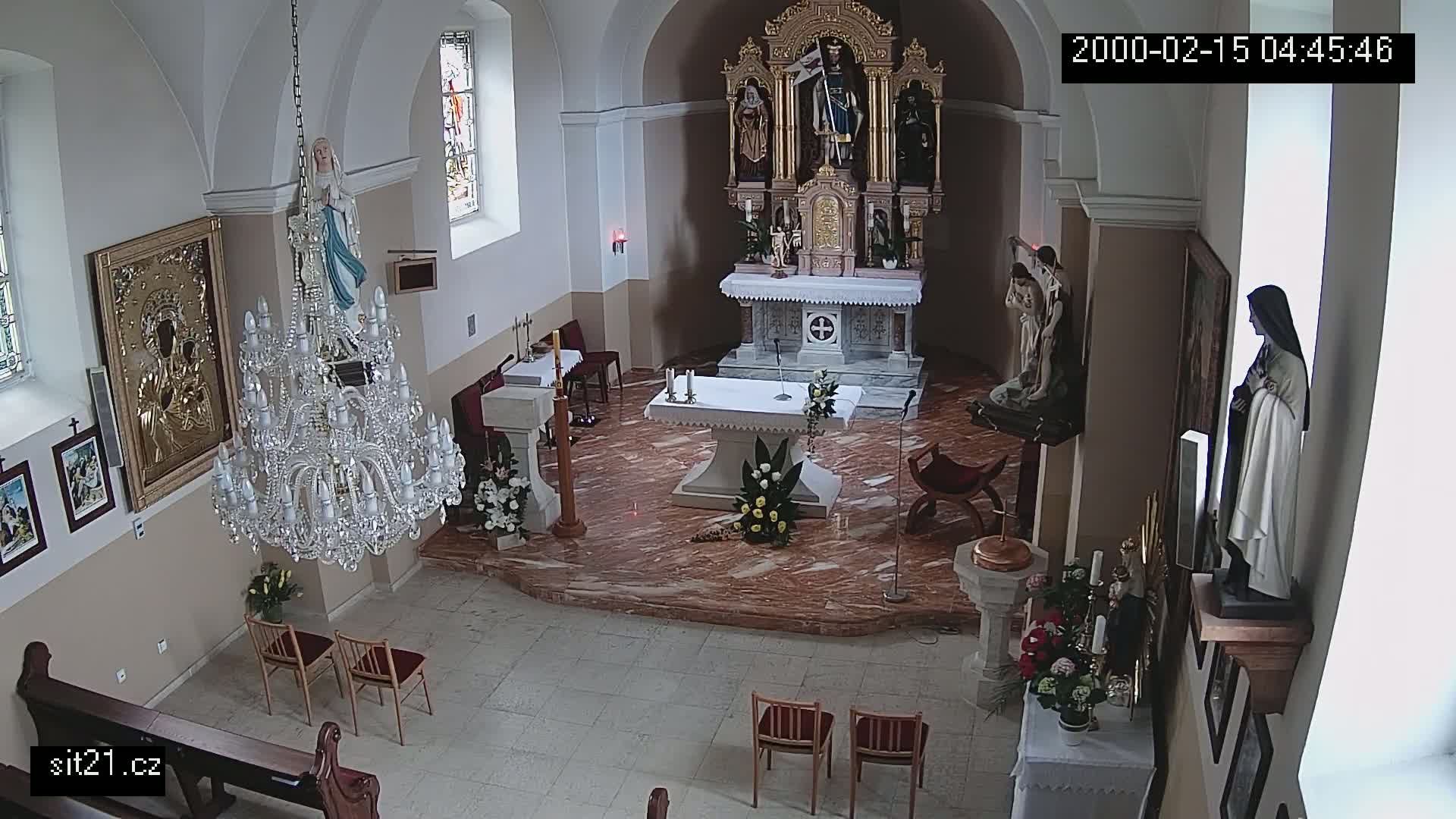 An indoor view of a church sanctuary, featuring an altar, religious statues, a chandelier, and several chairs arranged on a marble floor.