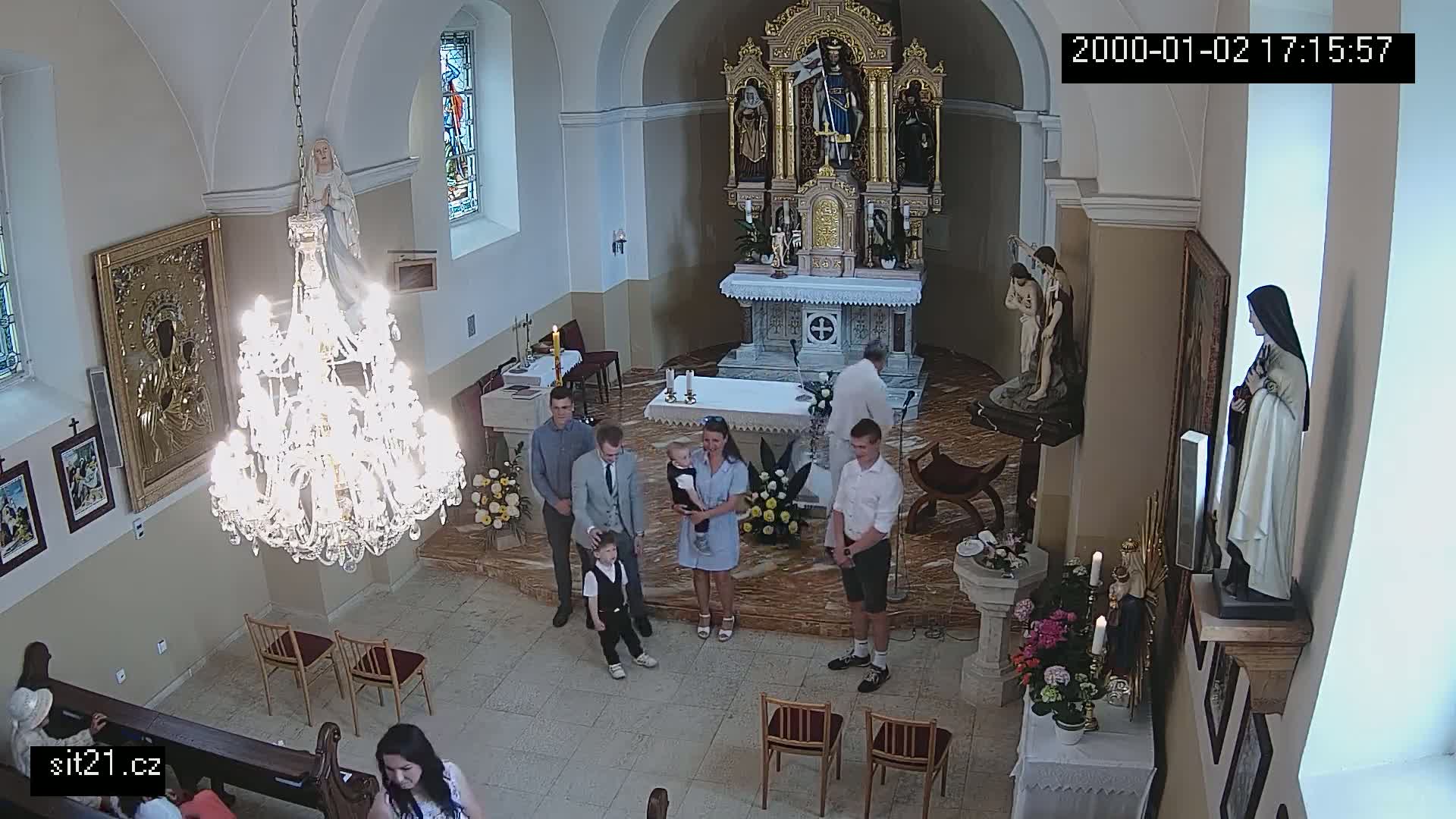 A family stands in a church during a ceremony, with a large chandelier hanging overhead.