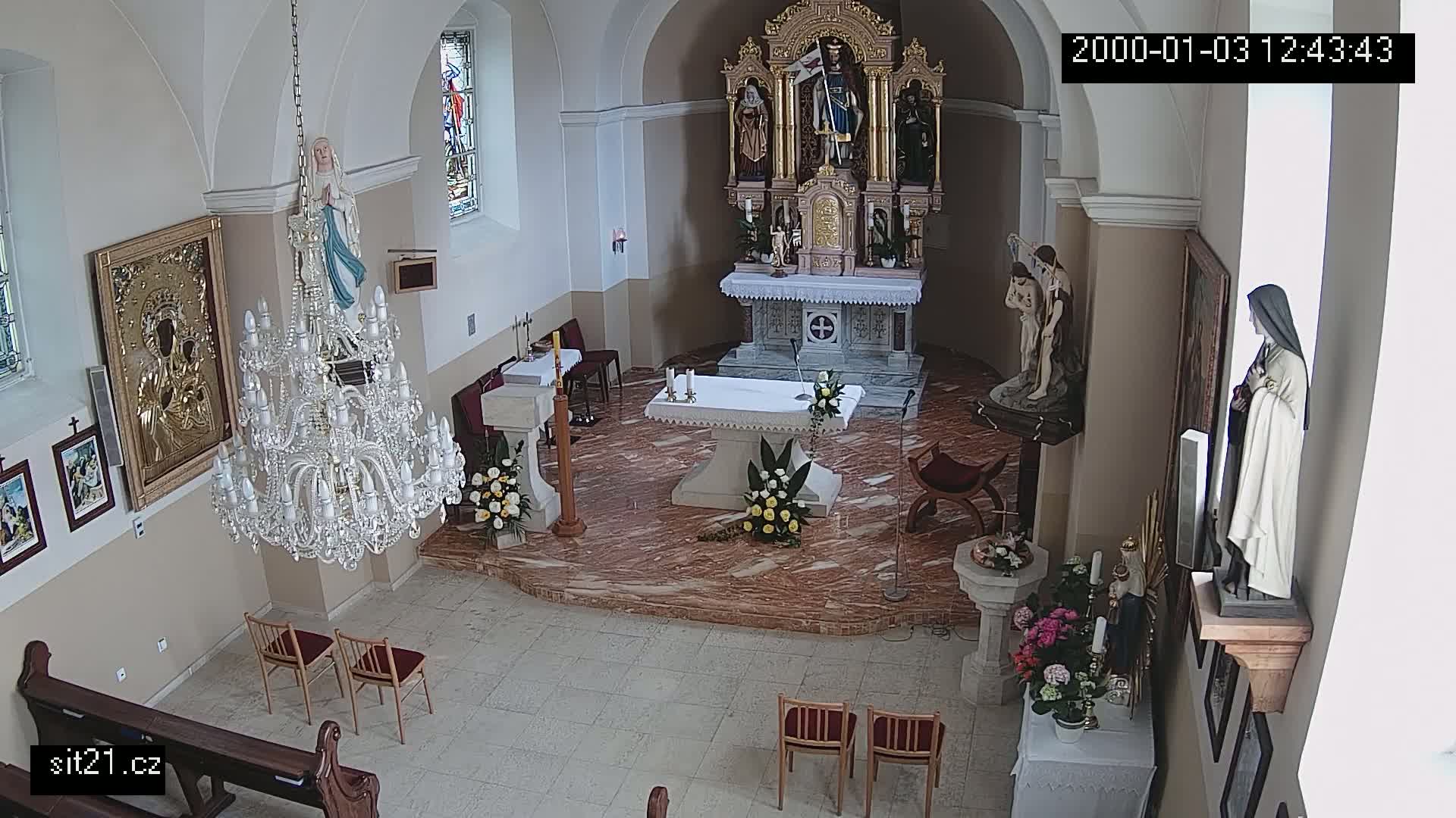 An indoor view of a church sanctuary, showing an altar, statues, a chandelier, and floral arrangements.
