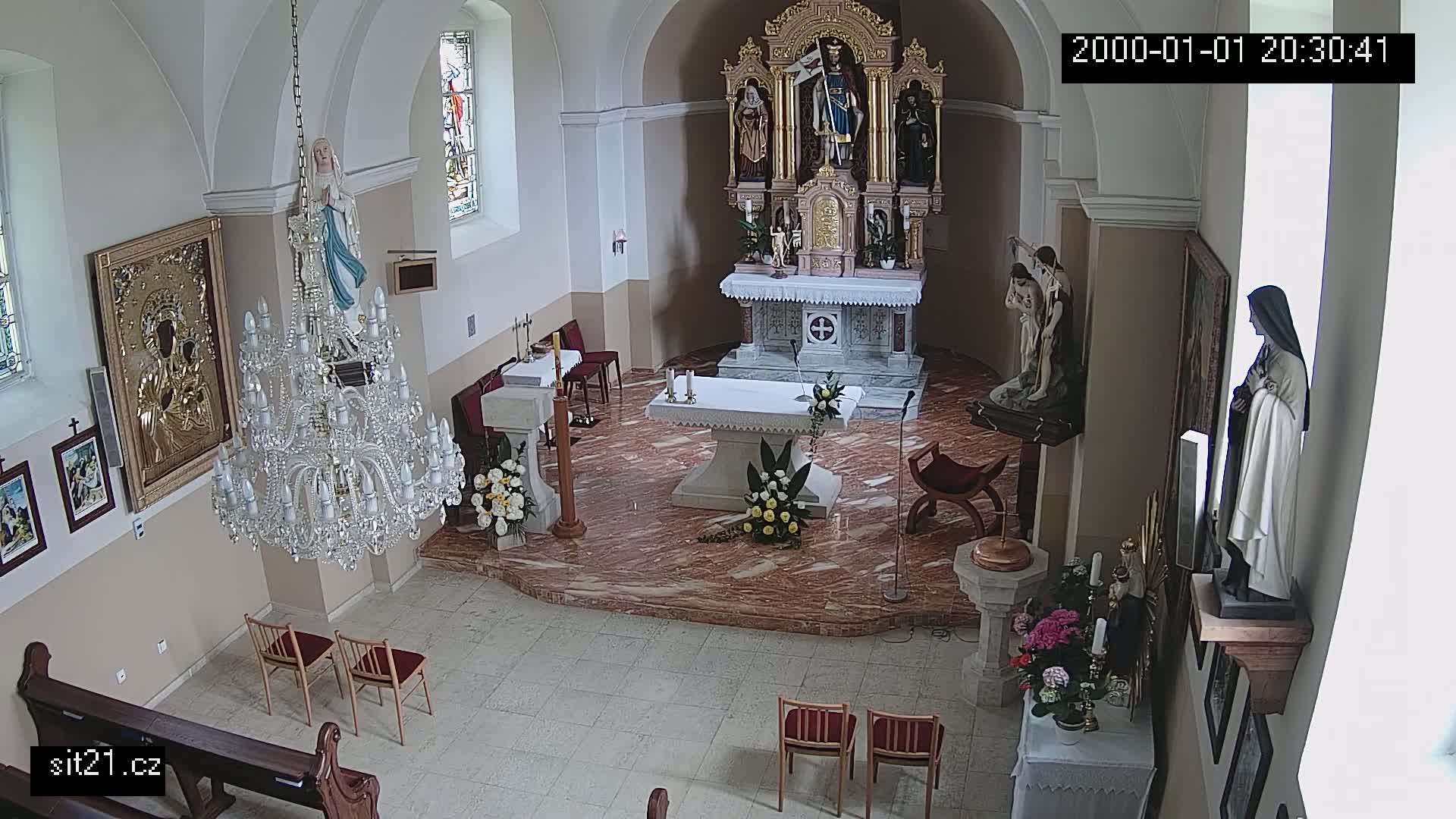 An indoor view of a church sanctuary, showing an altar, several statues, a large crystal chandelier, and floral arrangements.