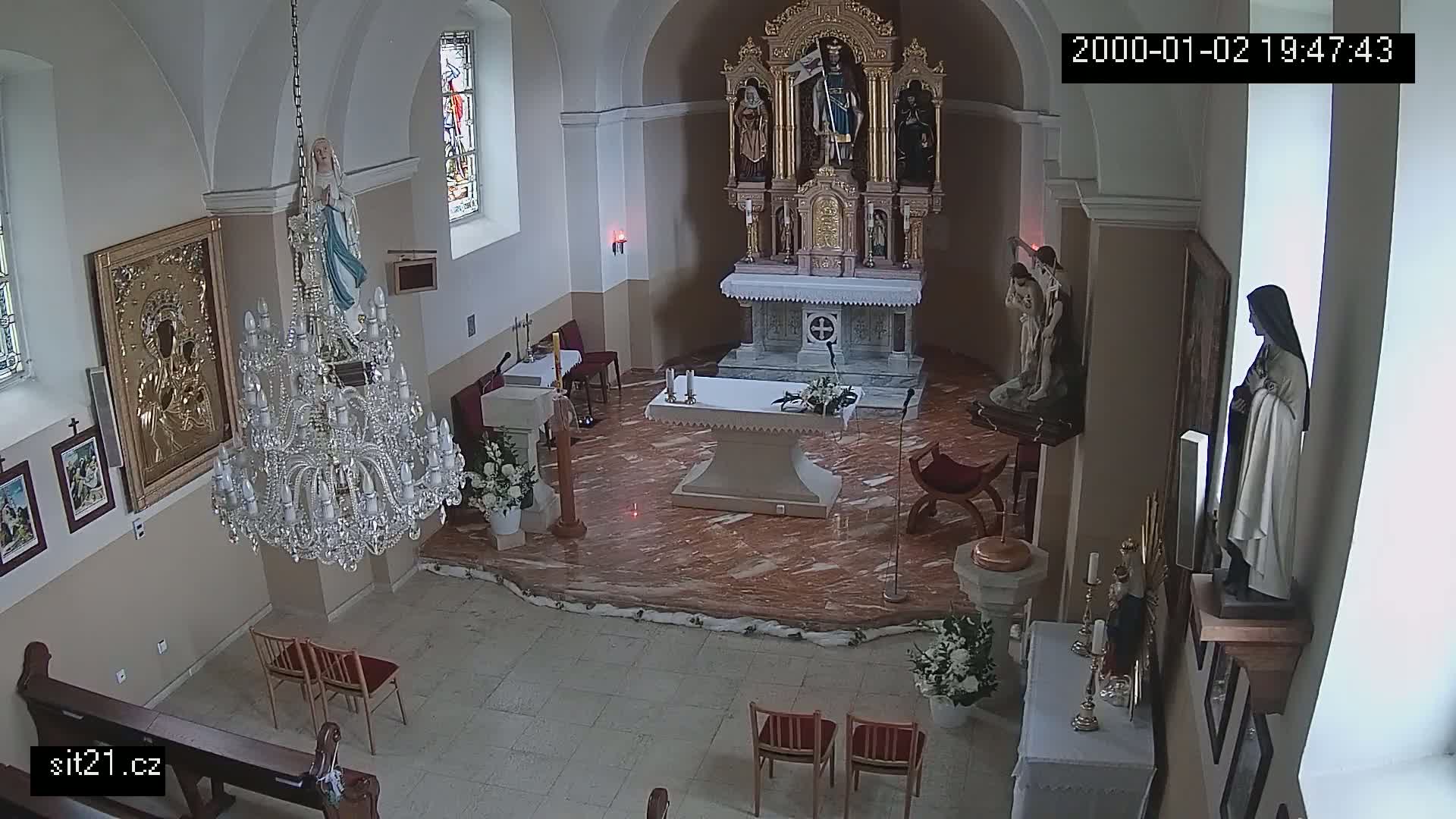 An indoor church sanctuary with marble floors, religious statues, and a large crystal chandelier is shown.
