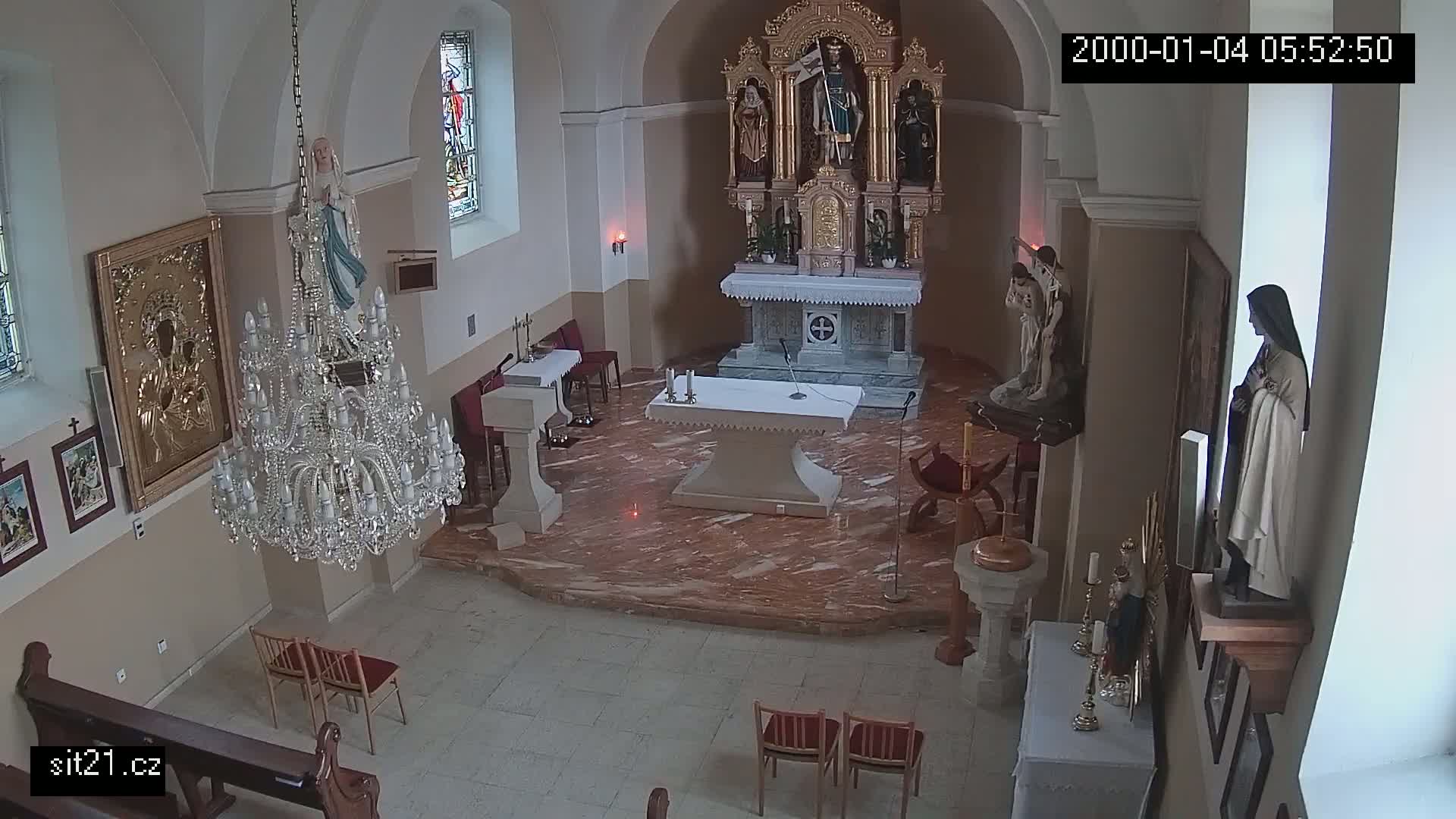 An indoor view of a church sanctuary with marble flooring, religious statues, a large chandelier, and several chairs.