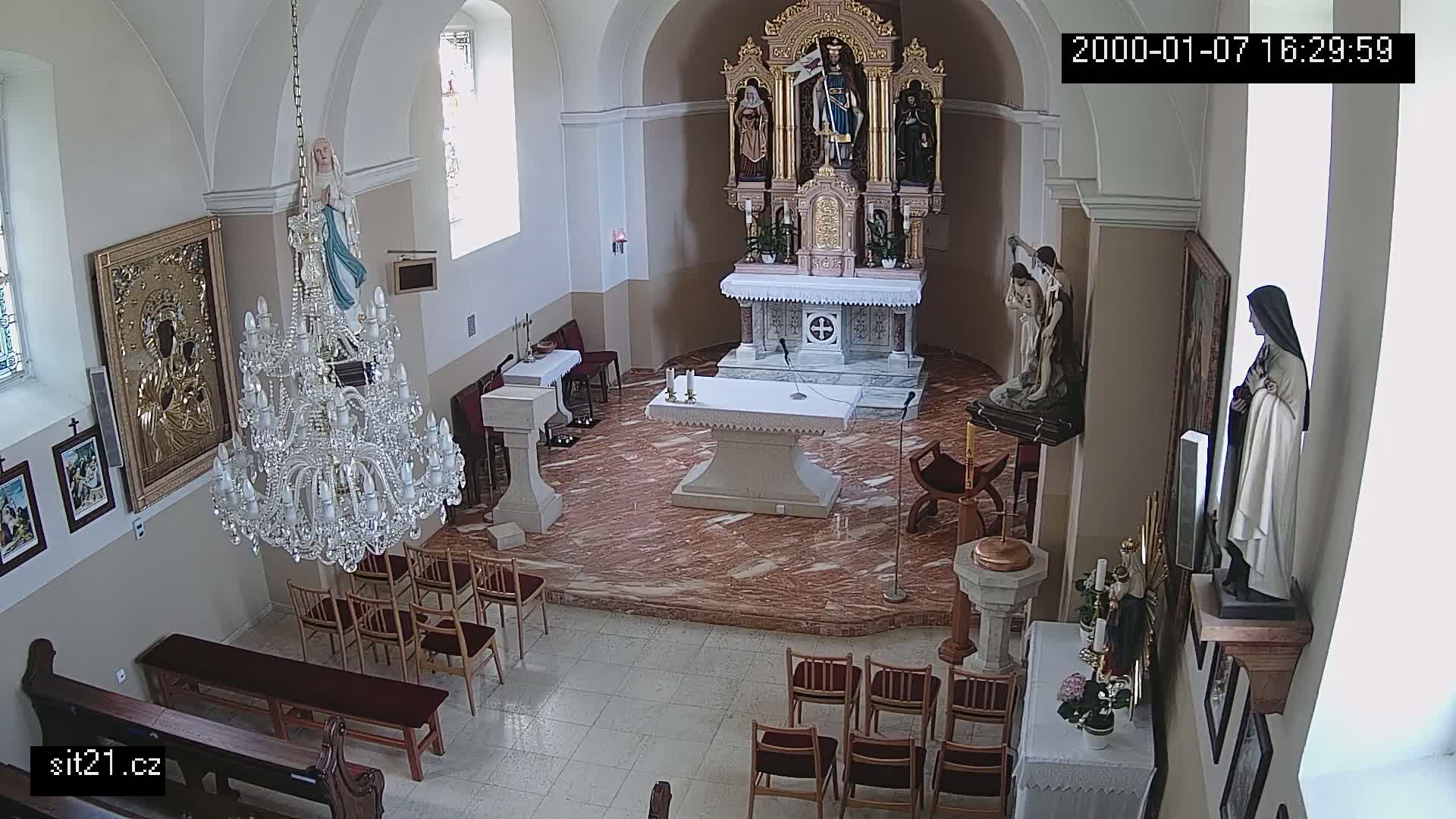An overhead view shows the interior of a church with an altar, statues, a chandelier, and rows of empty chairs on a marble floor.