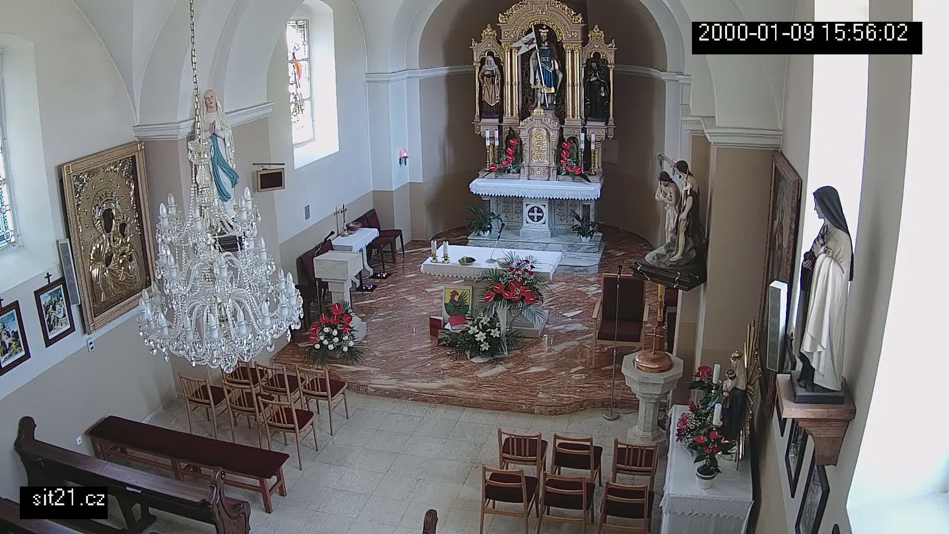 An indoor view of a church sanctuary, showing an altar, statues, a large chandelier, and rows of empty chairs.
