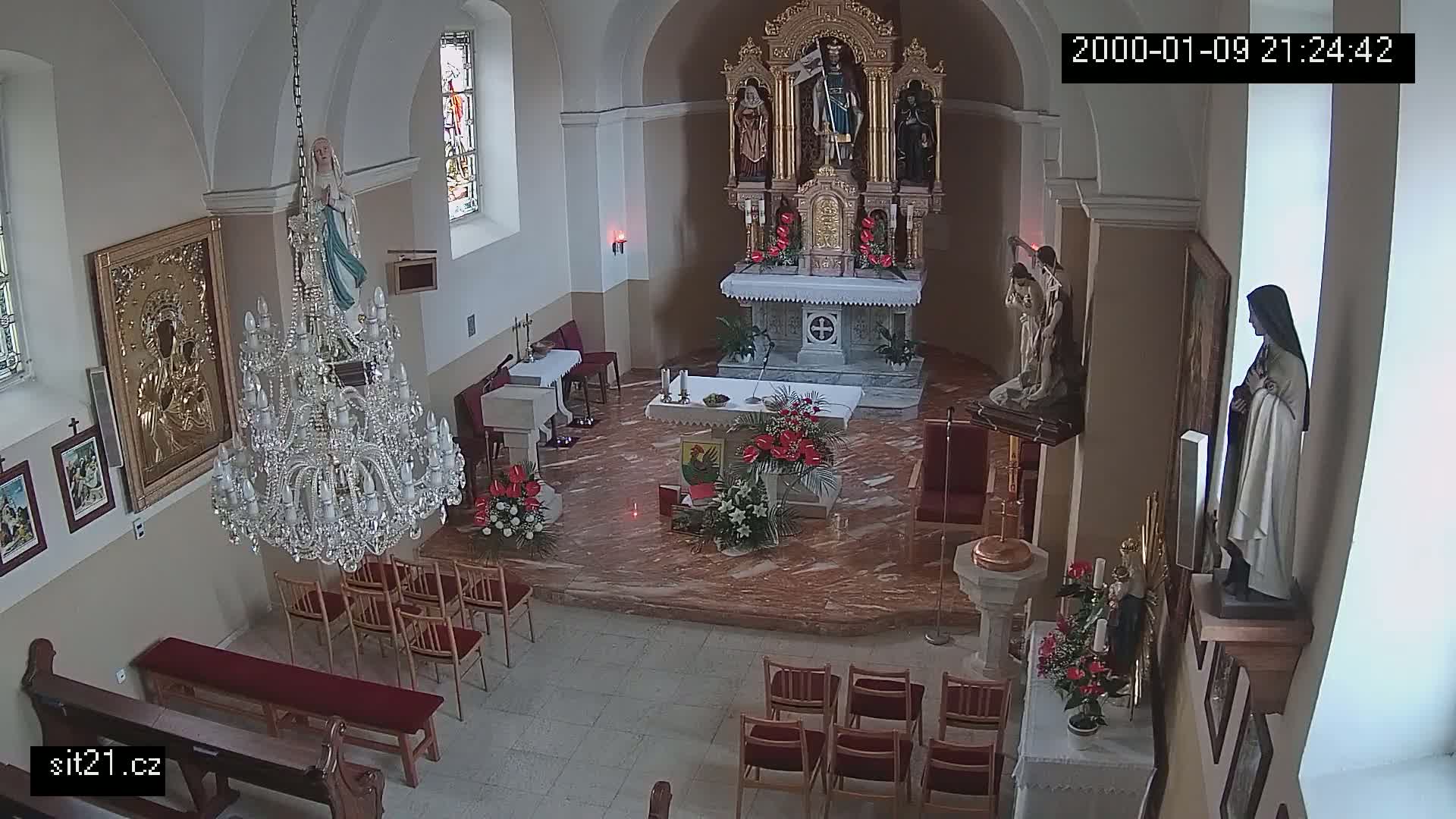 An indoor view of a church sanctuary, showing an altar, statues, a large chandelier, and rows of empty chairs.