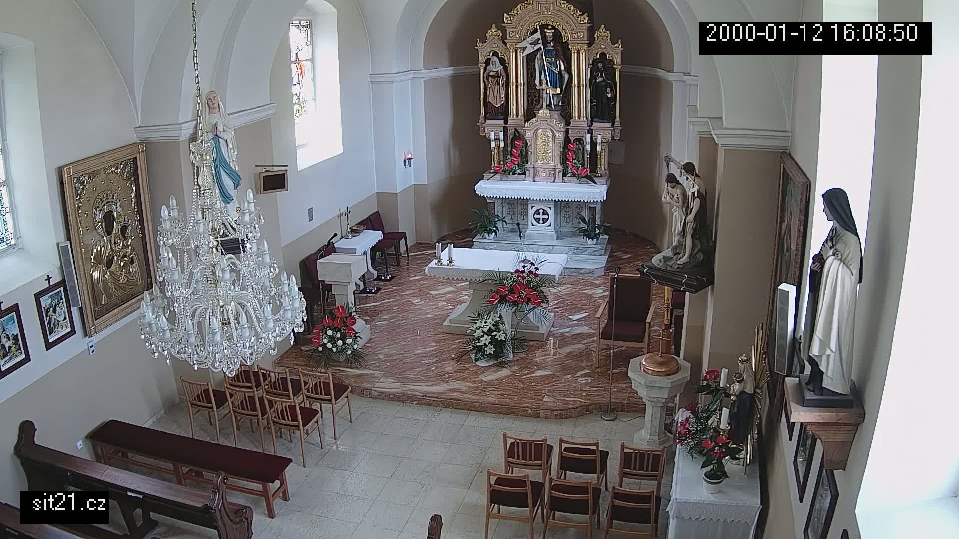 An indoor view of a church sanctuary with a marble floor, ornate altar, several religious statues, a large crystal chandelier, and rows of empty chairs.