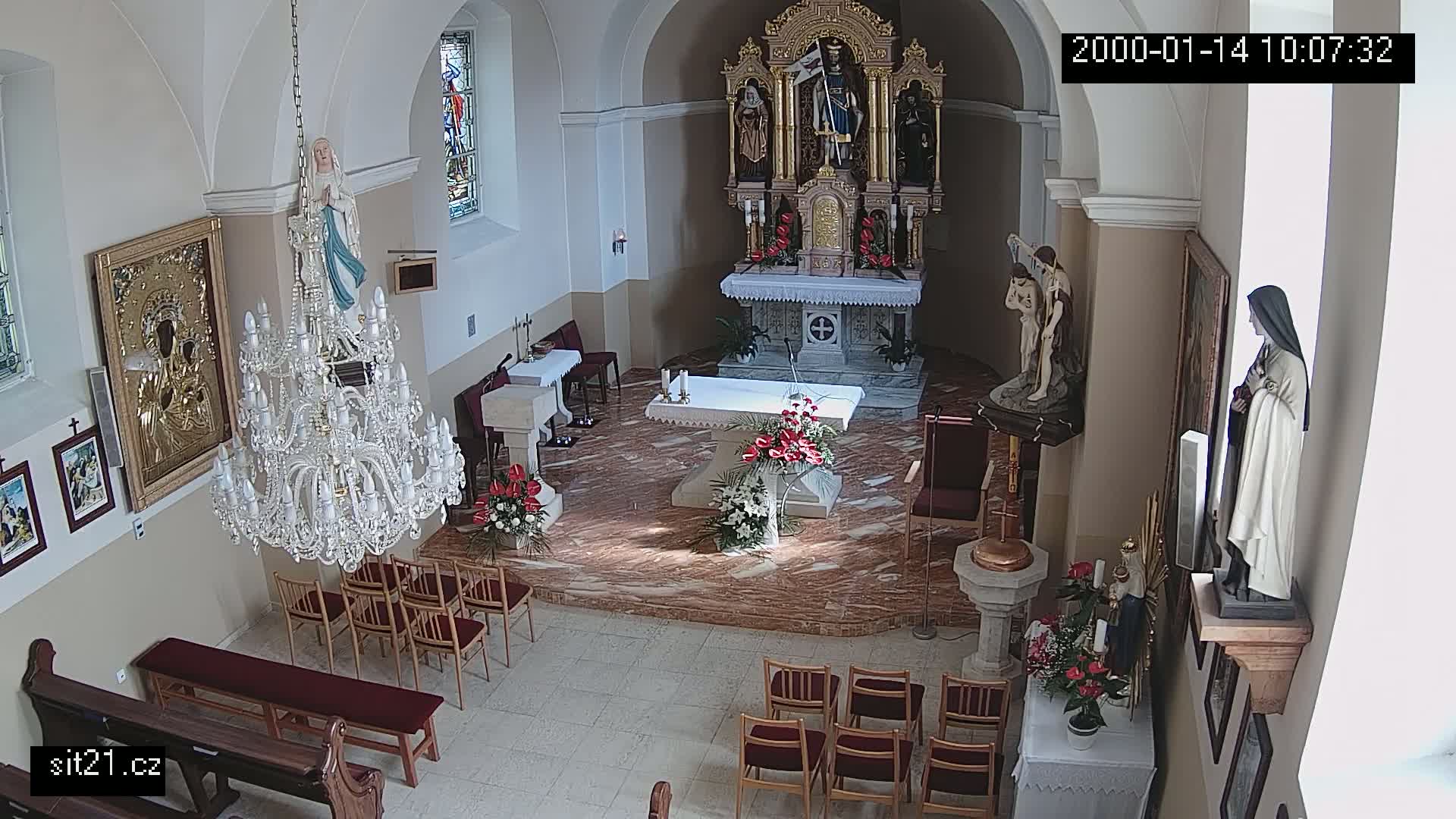 A church interior with marble floors, an altar adorned with flowers, a large crystal chandelier, and several religious statues and icons.